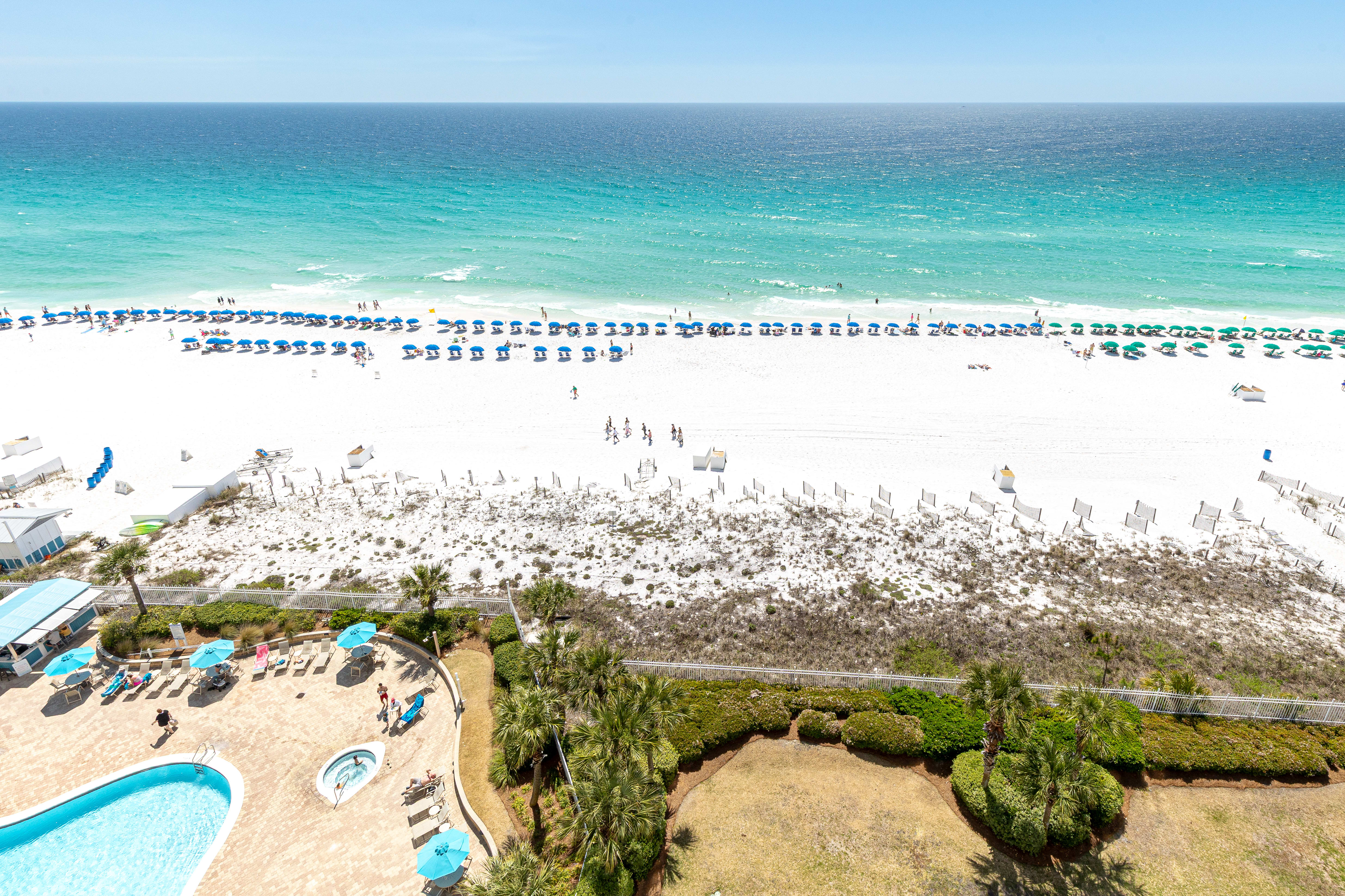 Stunning aerial view showcases pristine white sand beach with crystal-clear turquoise waters and organized beach umbrella rows stretching along the coastline.