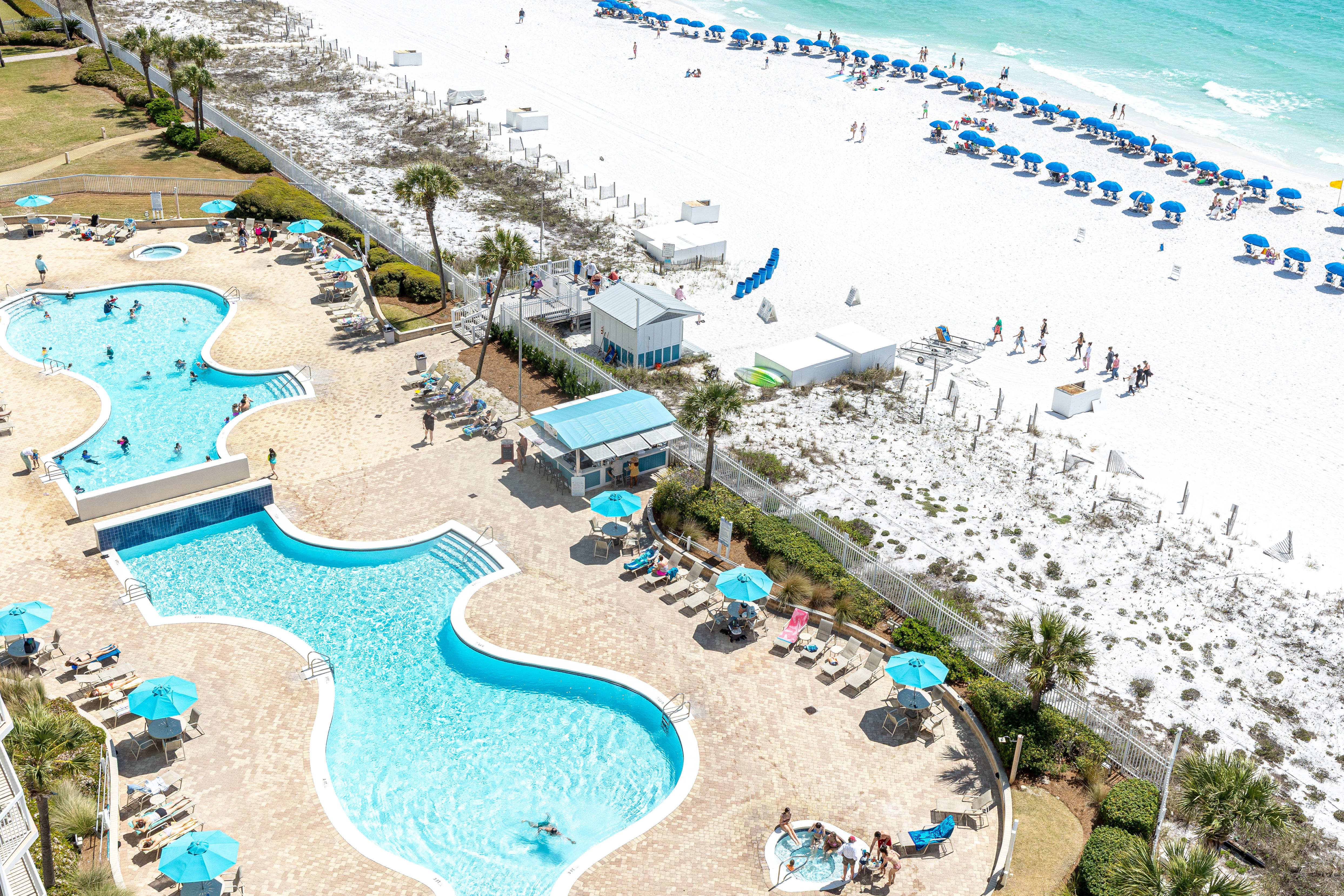 Beachfront resort with multi-level pools, white sand beach, and turquoise waters stretching to the horizon.