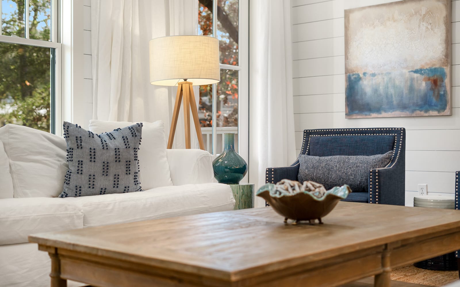 Relax in your bright living space with comfortable seating, coastal artwork, and natural light streaming through large windows.