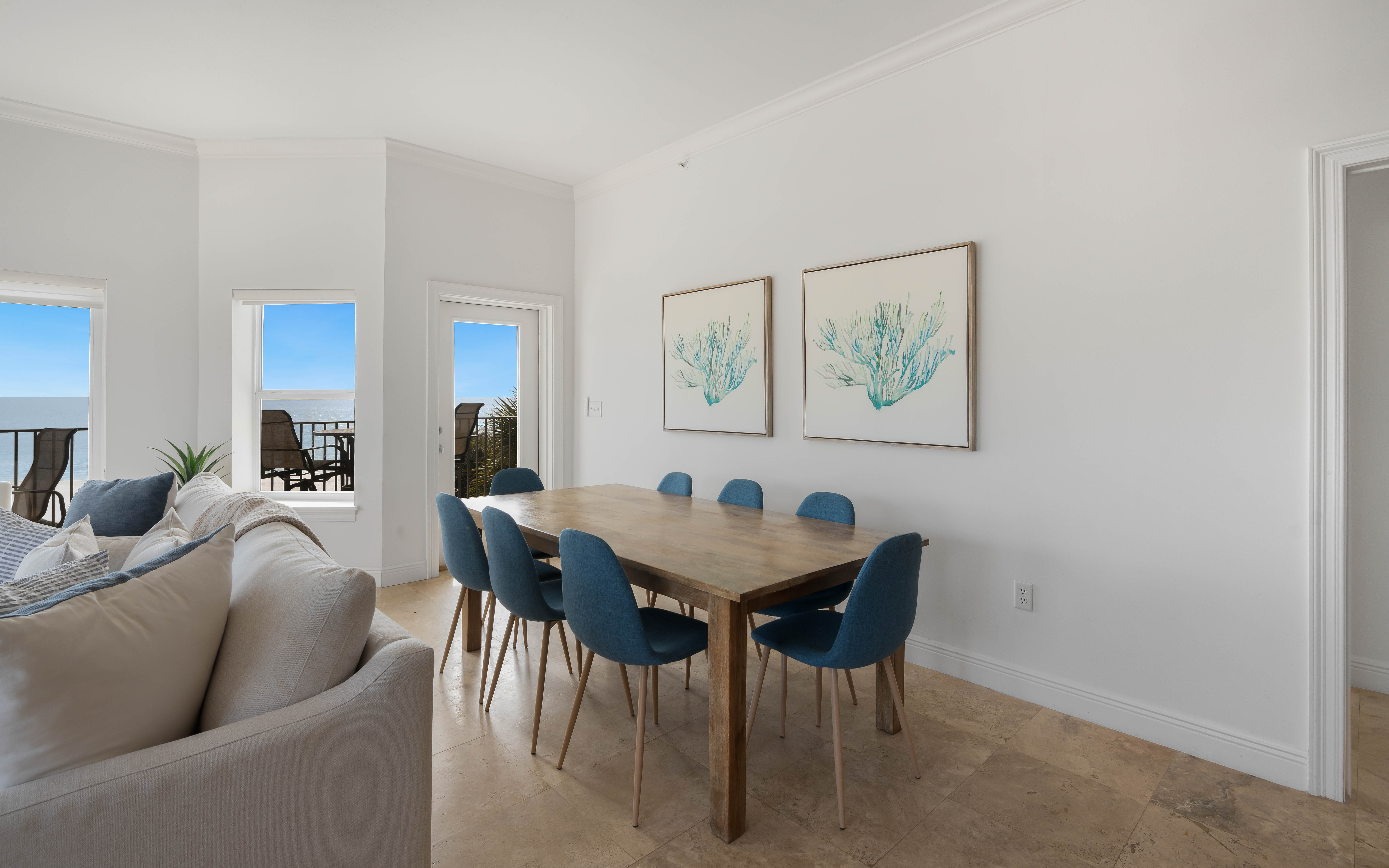 Your bright dining space opens to stunning gulf views through floor-to-ceiling windows, where coastal artwork complements the serene blue palette.