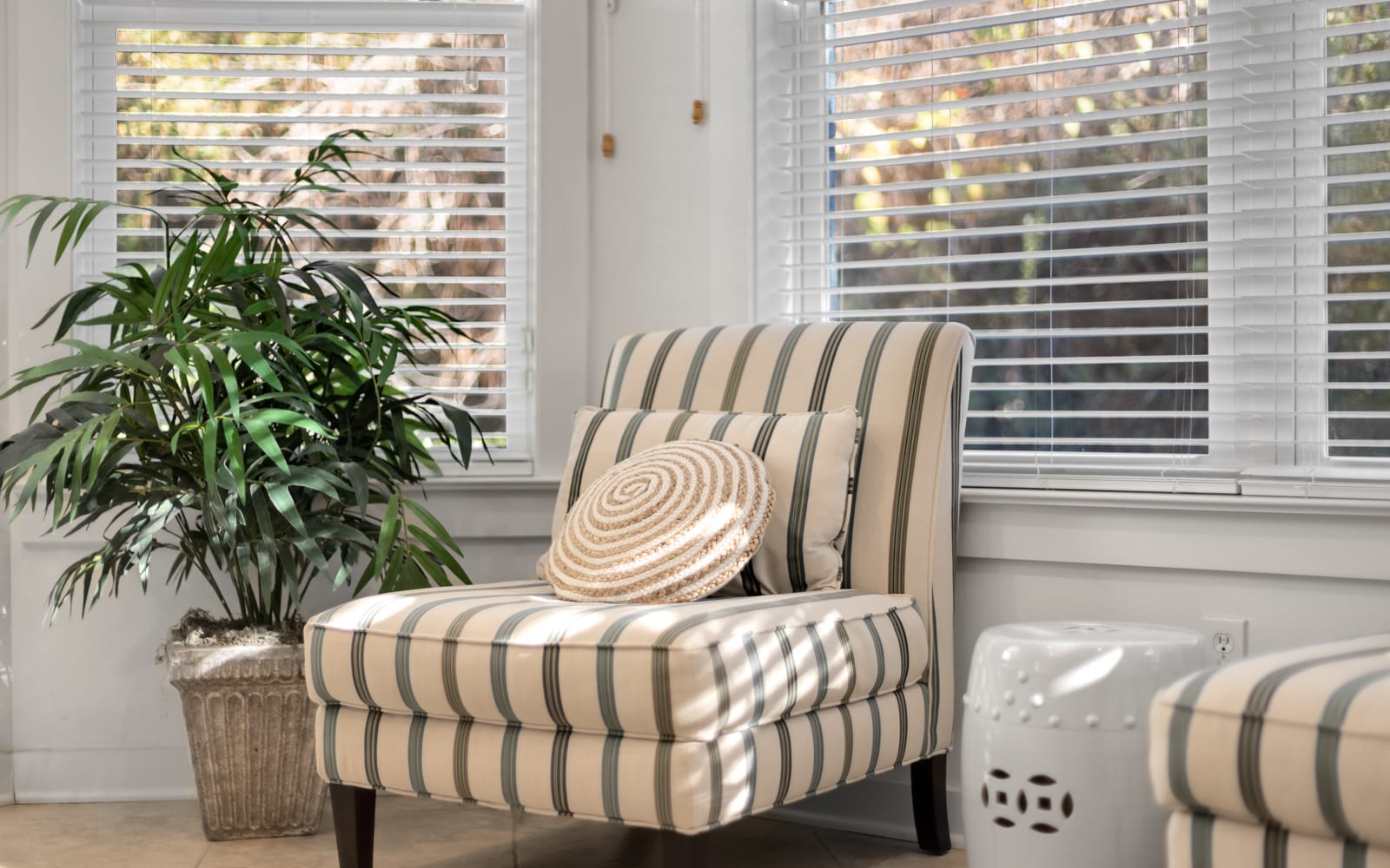 Settle into your private reading nook by bright windows, where natural light filters through blinds onto a comfy striped chair.