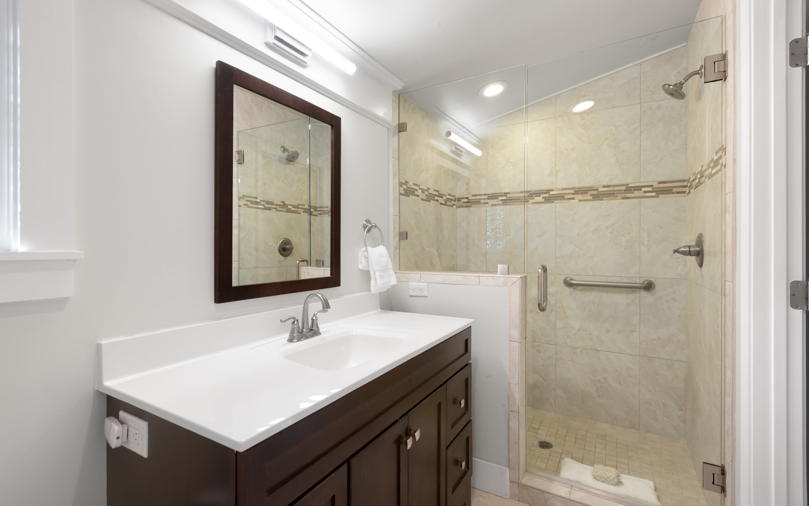 Your private bathroom features elegant white countertops, warm wood cabinetry, and a spacious glass-enclosed shower with beautiful tile details.