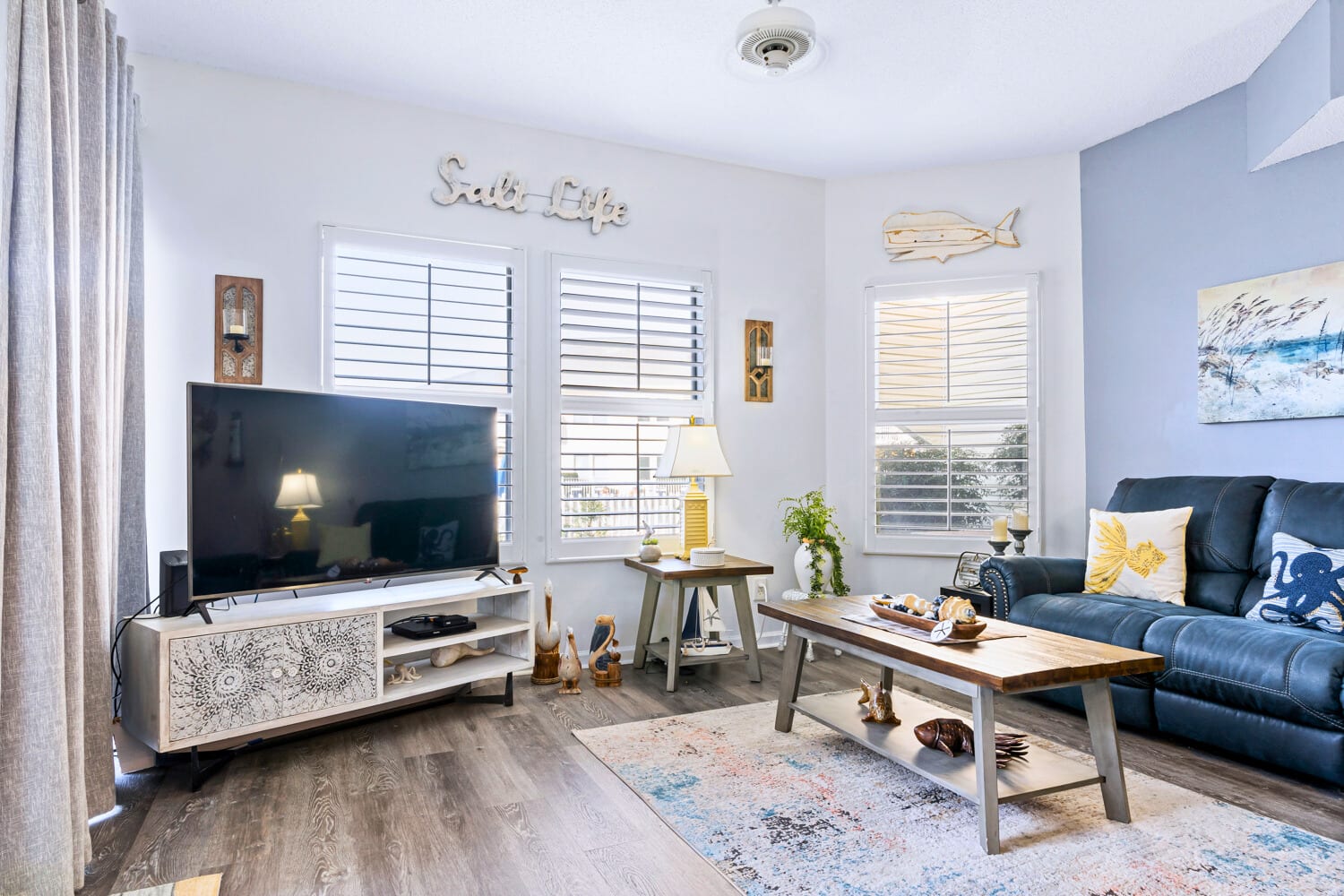 Unwind in your coastal-themed living room with plush seating, charming nautical touches, and natural light streaming through plantation shutters.