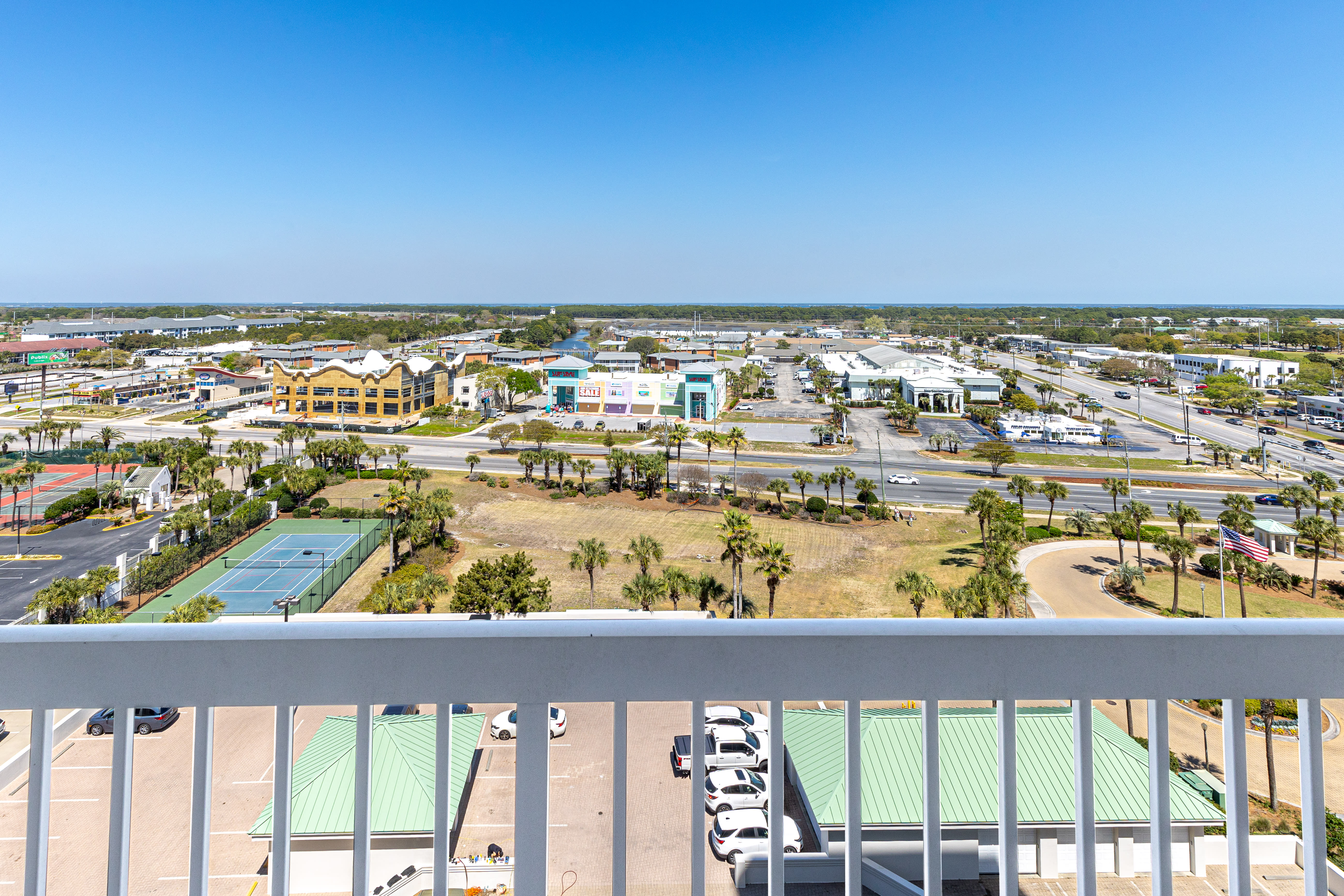 Elevated view from balcony overlooking tennis courts, palm trees, and the vibrant town center below.