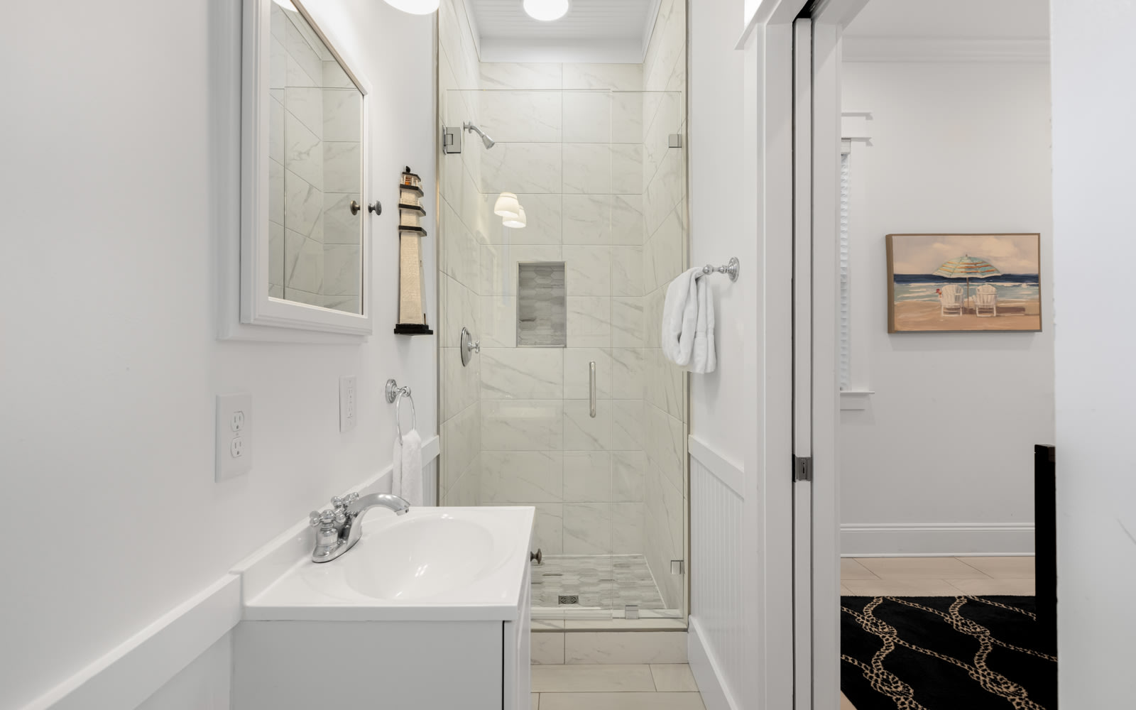 Step into your pristine bathroom with marble shower, fresh towels, and coastal artwork creating a spa-like retreat.