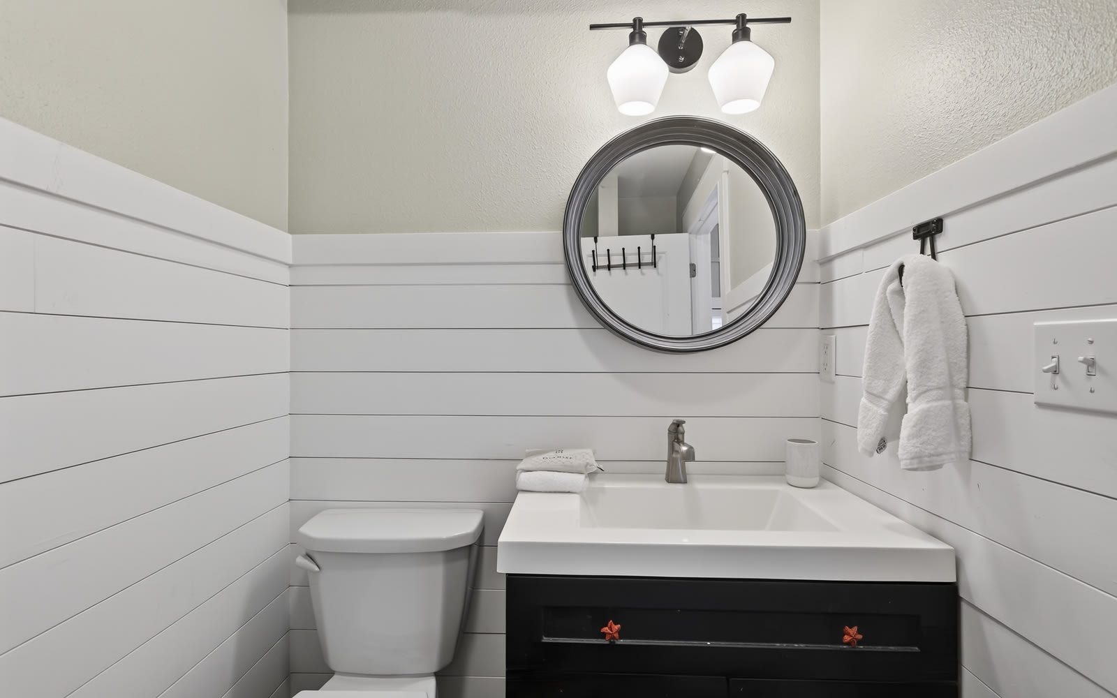 Your pristine powder room features modern farmhouse charm with crisp white shiplap walls, elegant lighting, and thoughtful amenities.