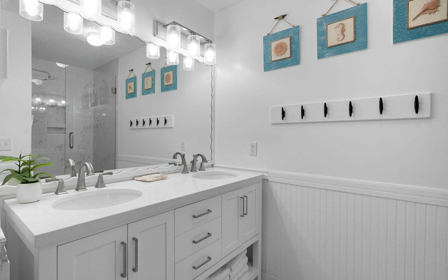 Step into your coastal-themed bathroom featuring dual vanities, elegant lighting, and beachy artwork that creates a spa-like retreat.