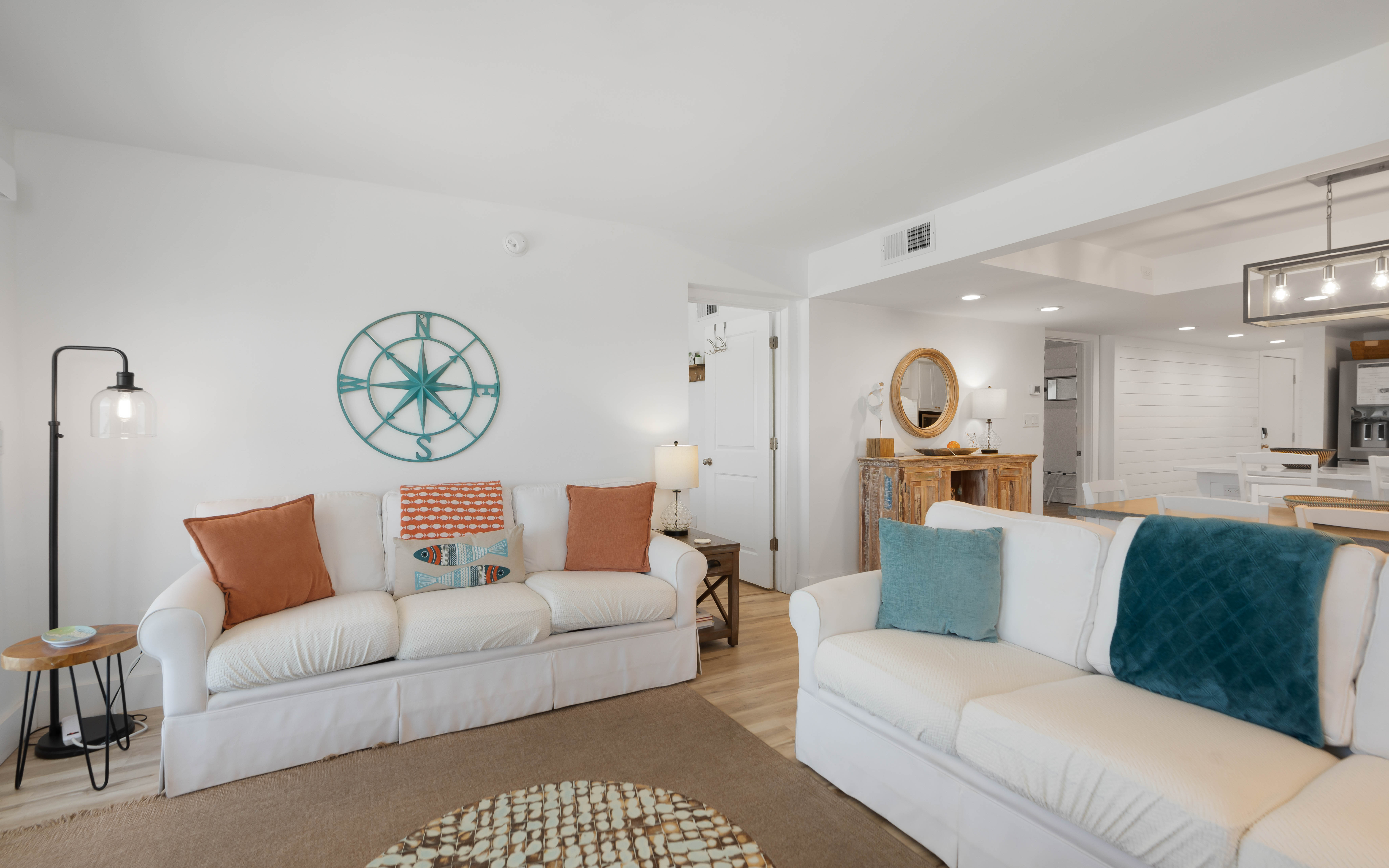 Sink into plush white sofas adorned with coastal-inspired pillows, where nautical charm meets modern comfort in your bright, airy retreat.