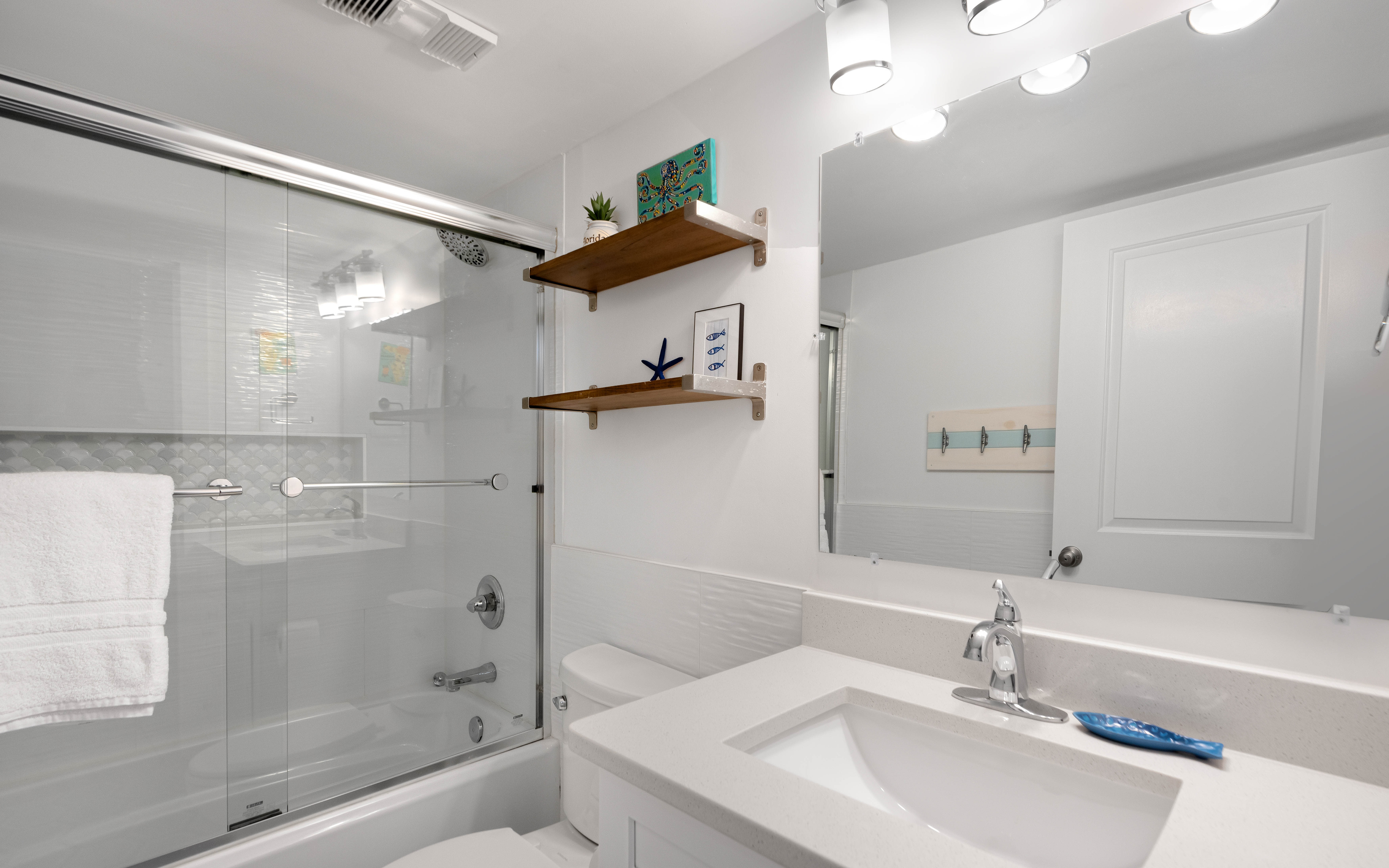 Unwind in your pristine bathroom featuring a glass-enclosed tub-shower combo and stylish vanity with thoughtful coastal touches.