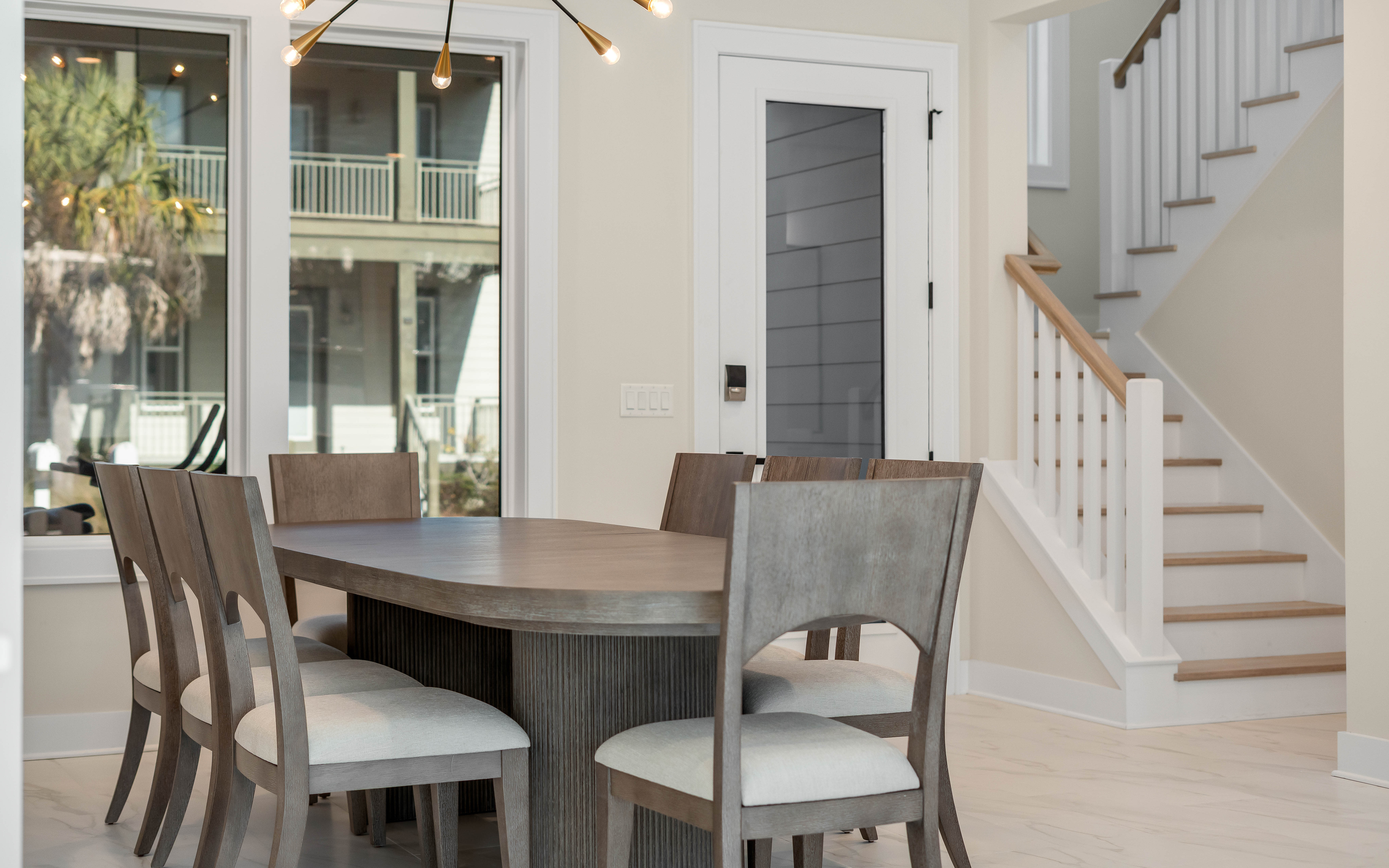 Gather around this elegant dining table for memorable meals, with natural light streaming through windows and a cozy staircase nearby.