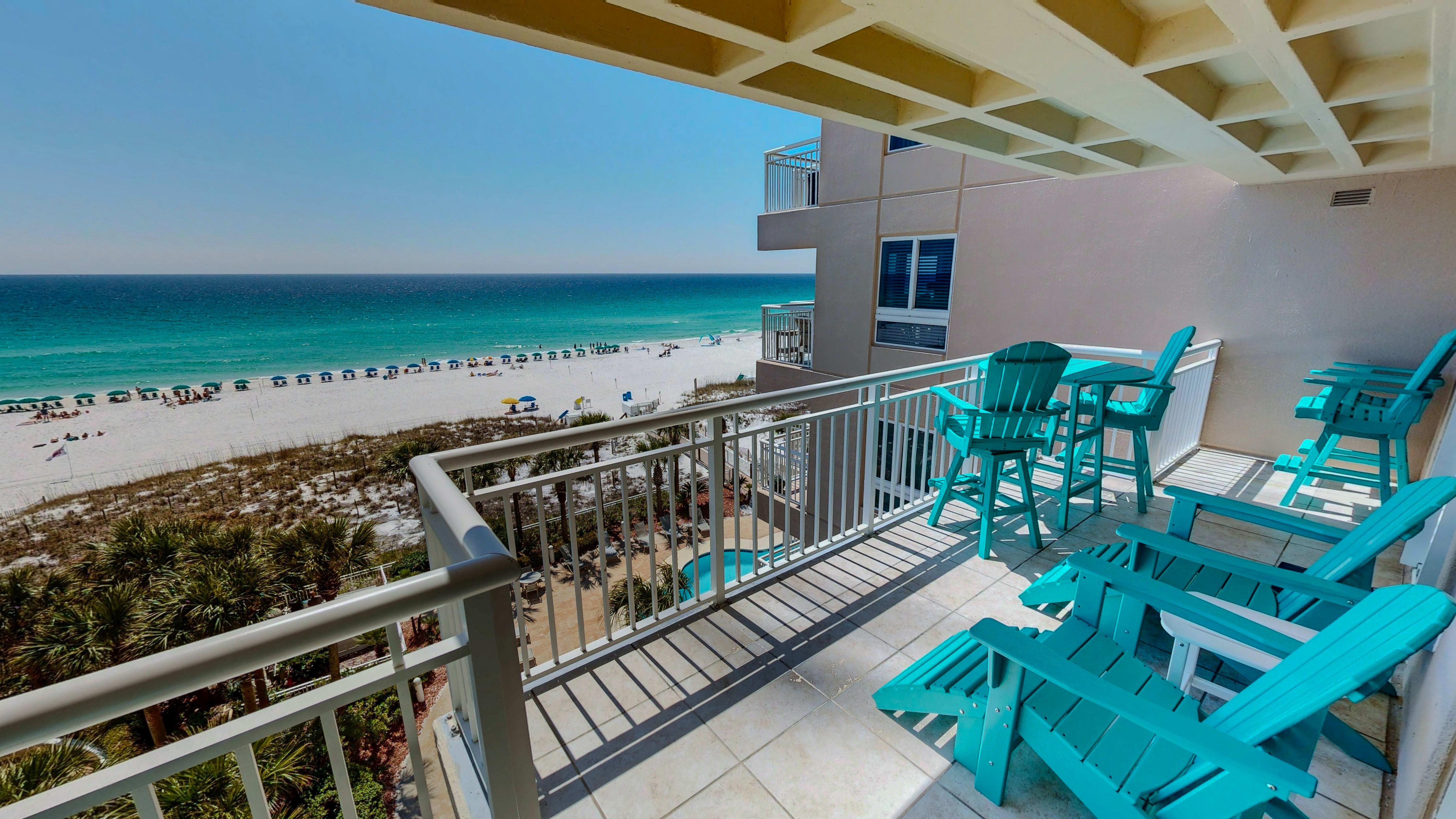 Stunning beachfront balcony with turquoise chairs overlooking pristine white sand and emerald waters. Your perfect retreat awaits.