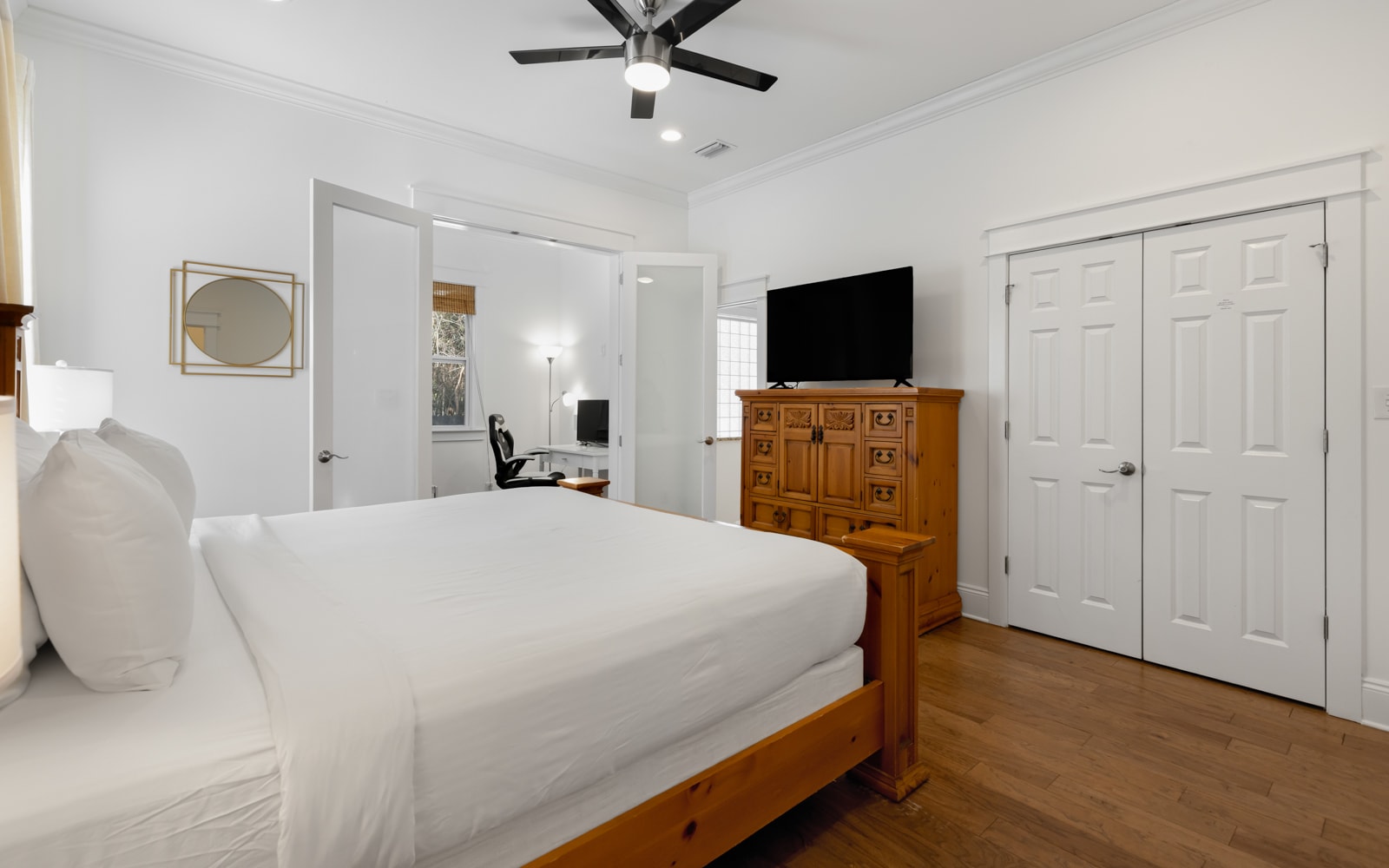 Unwind in your serene bedroom featuring crisp white linens, warm wood floors, and thoughtful touches like a ceiling fan for comfort.