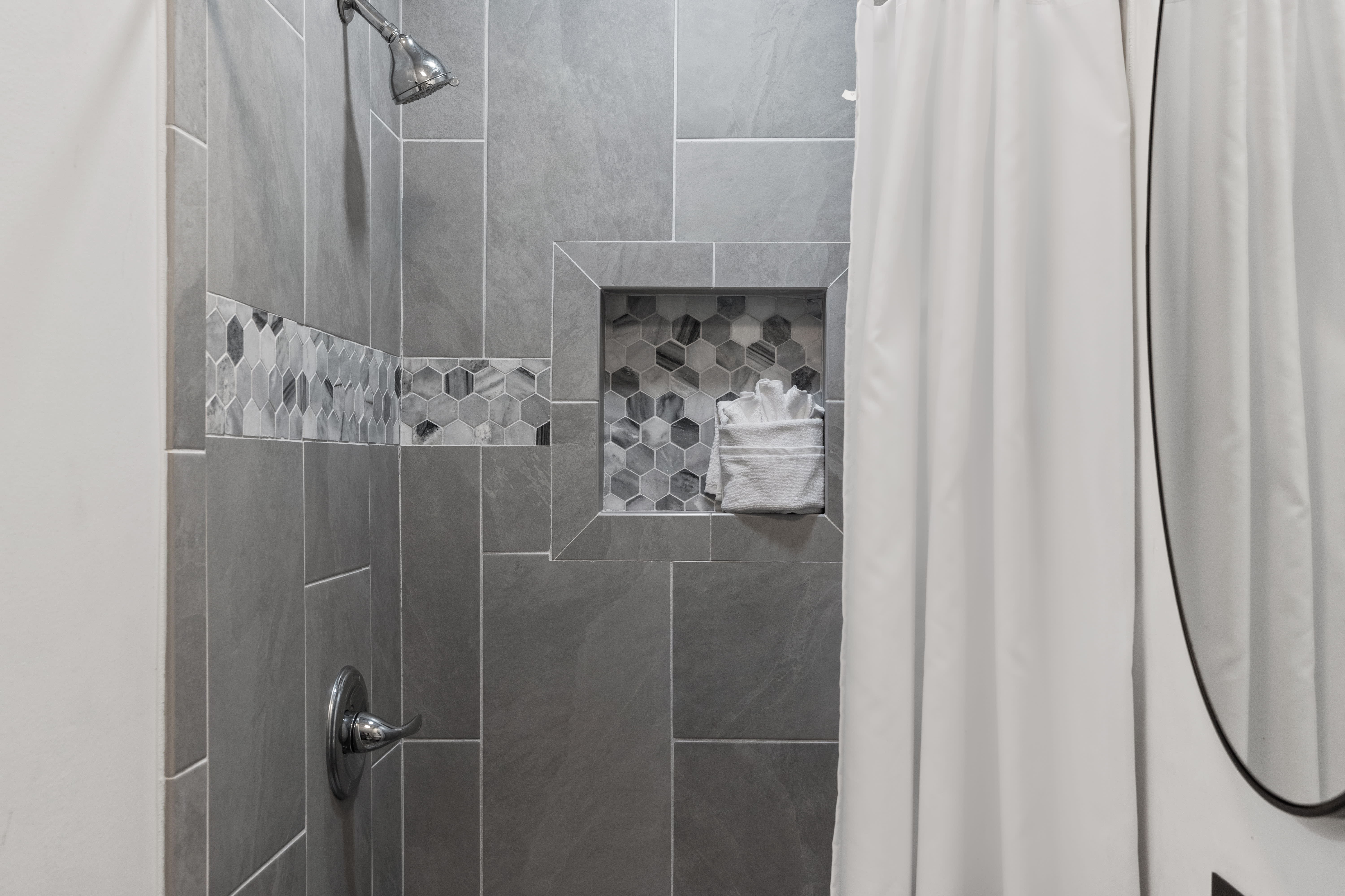 Step into your sleek tiled shower featuring modern gray tiles, hexagon accent details, and a convenient built-in niche for your toiletries.