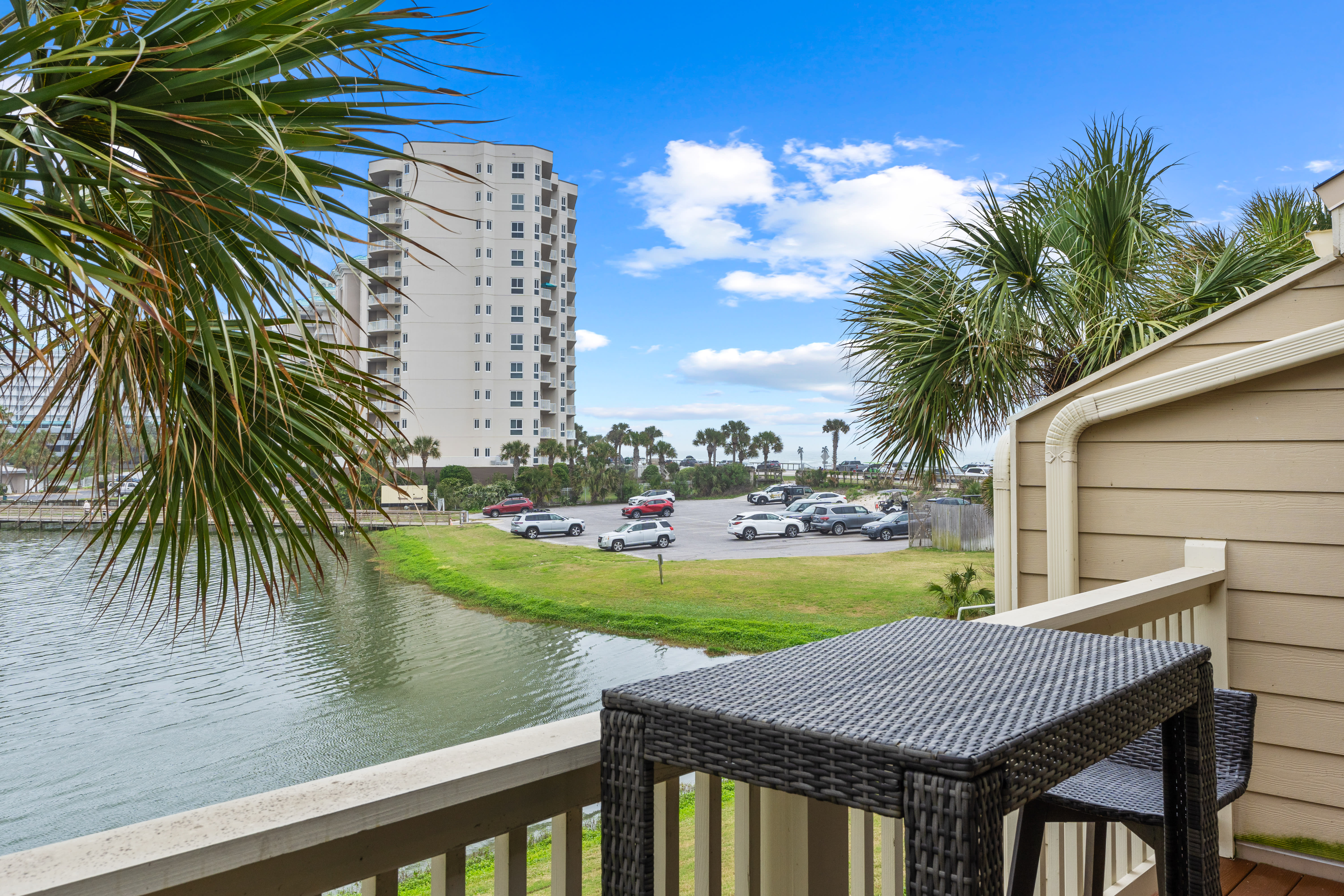 Waterfront property balcony overlooking a tropical canal with palm trees and coastal high-rise buildings visible across the water.