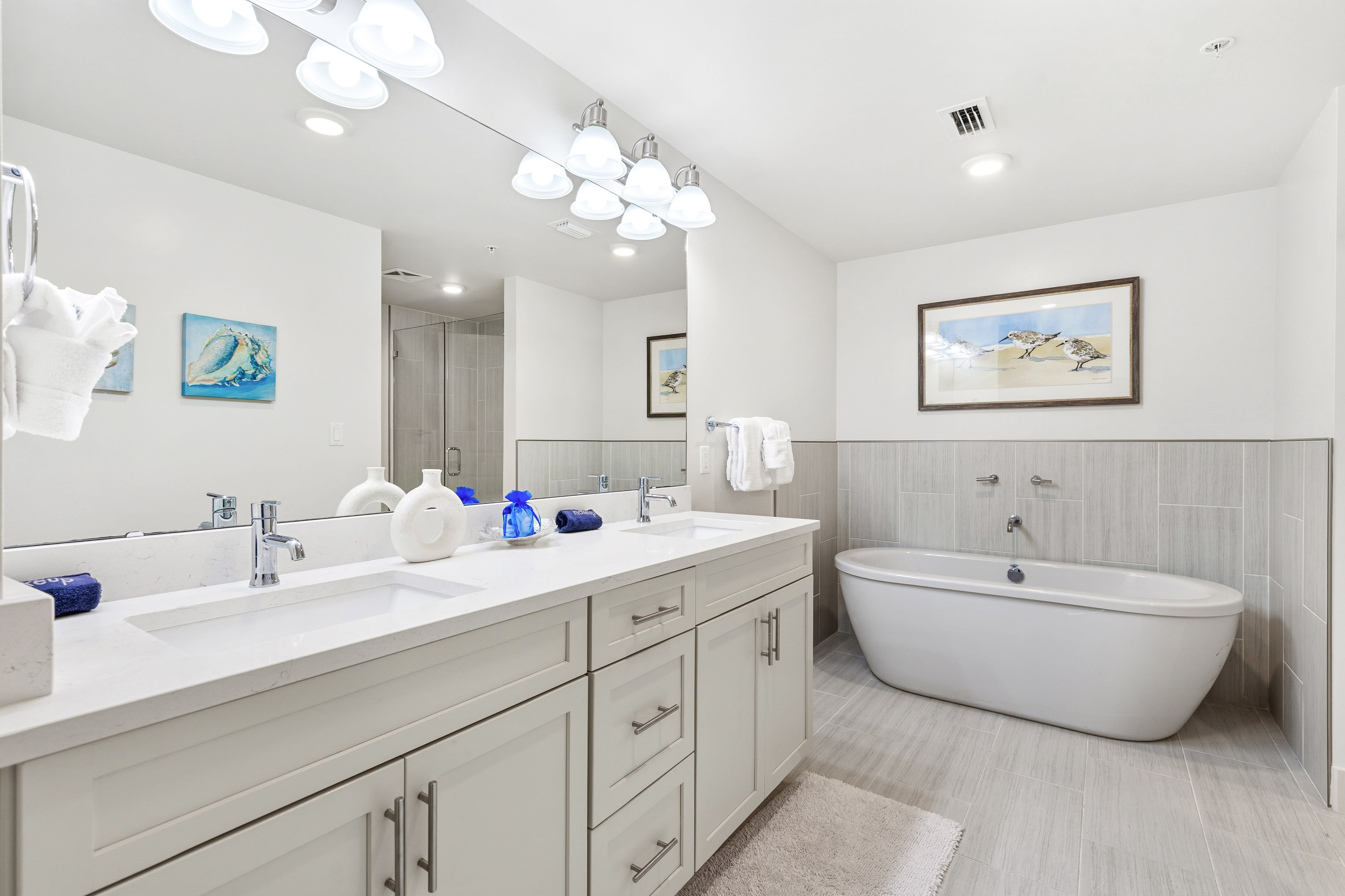 Indulge in your private spa-like bathroom featuring dual sinks, a luxurious soaking tub, and elegant coastal artwork that creates a serene retreat.