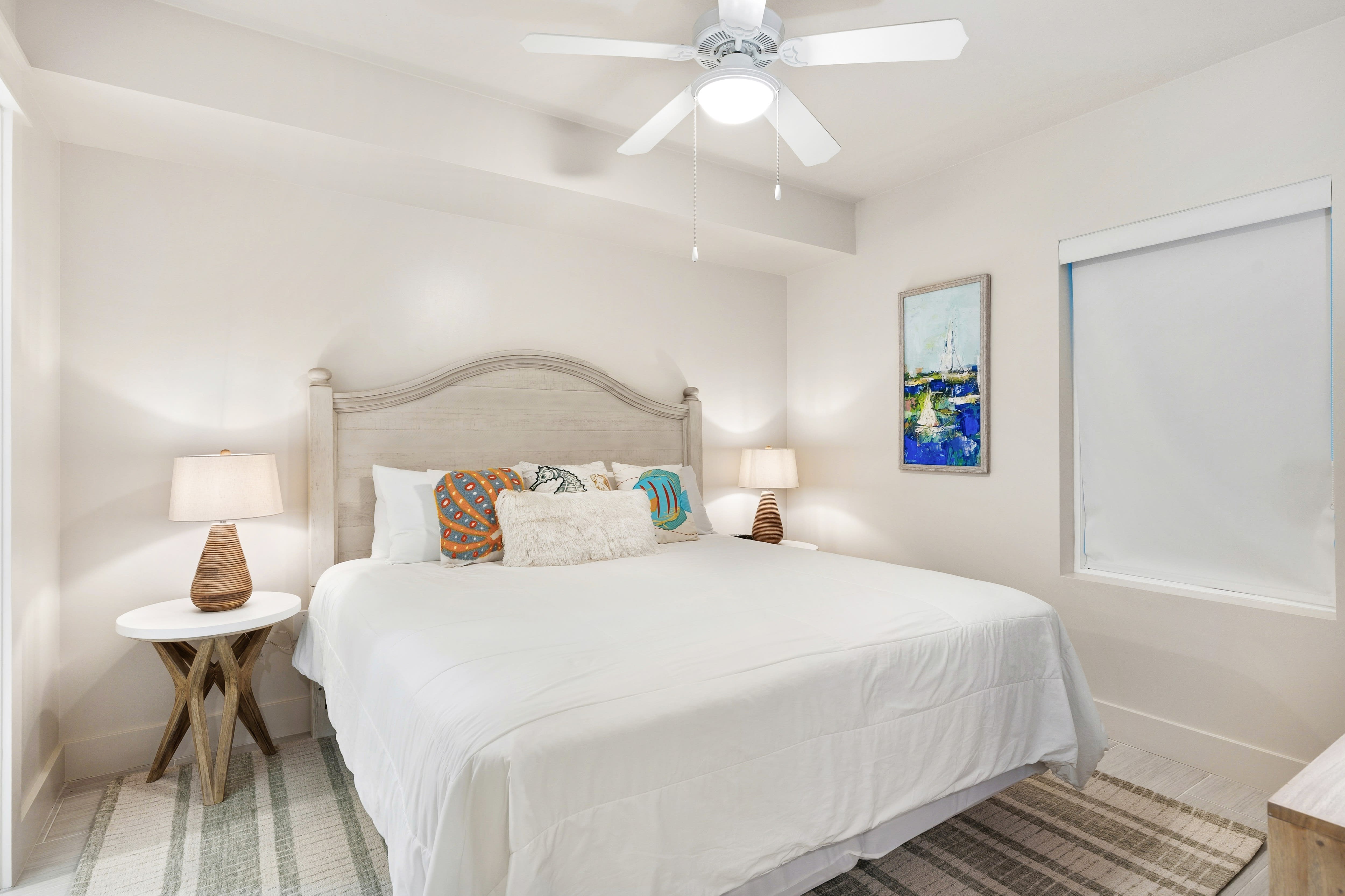 Sink into coastal comfort with crisp white linens, cheerful throw pillows, and a gentle ceiling fan to keep you cool.