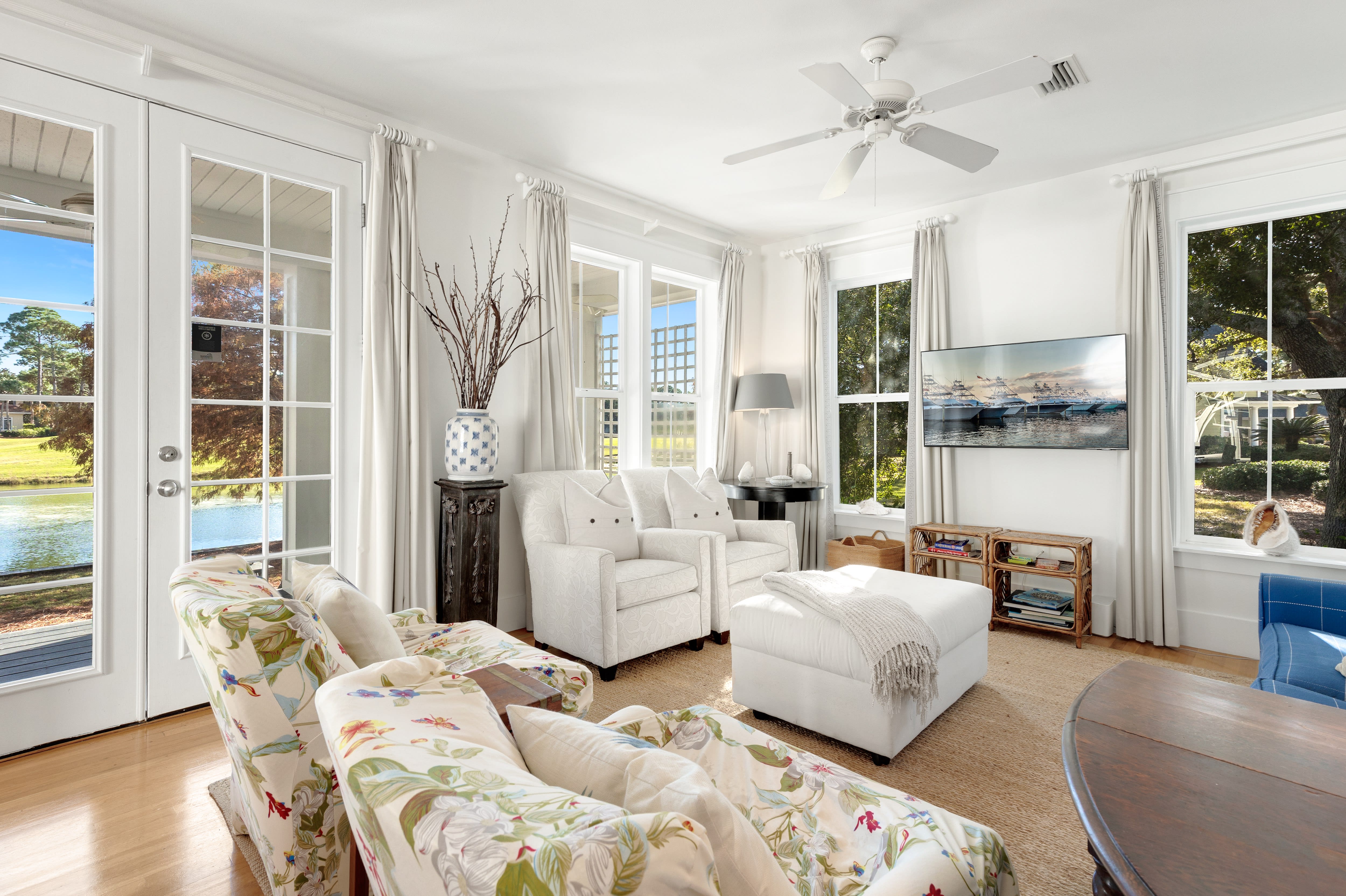 Sink into this sun-soaked living room where French doors reveal serene lake views and gentle breezes flow through your bright, coastal retreat.