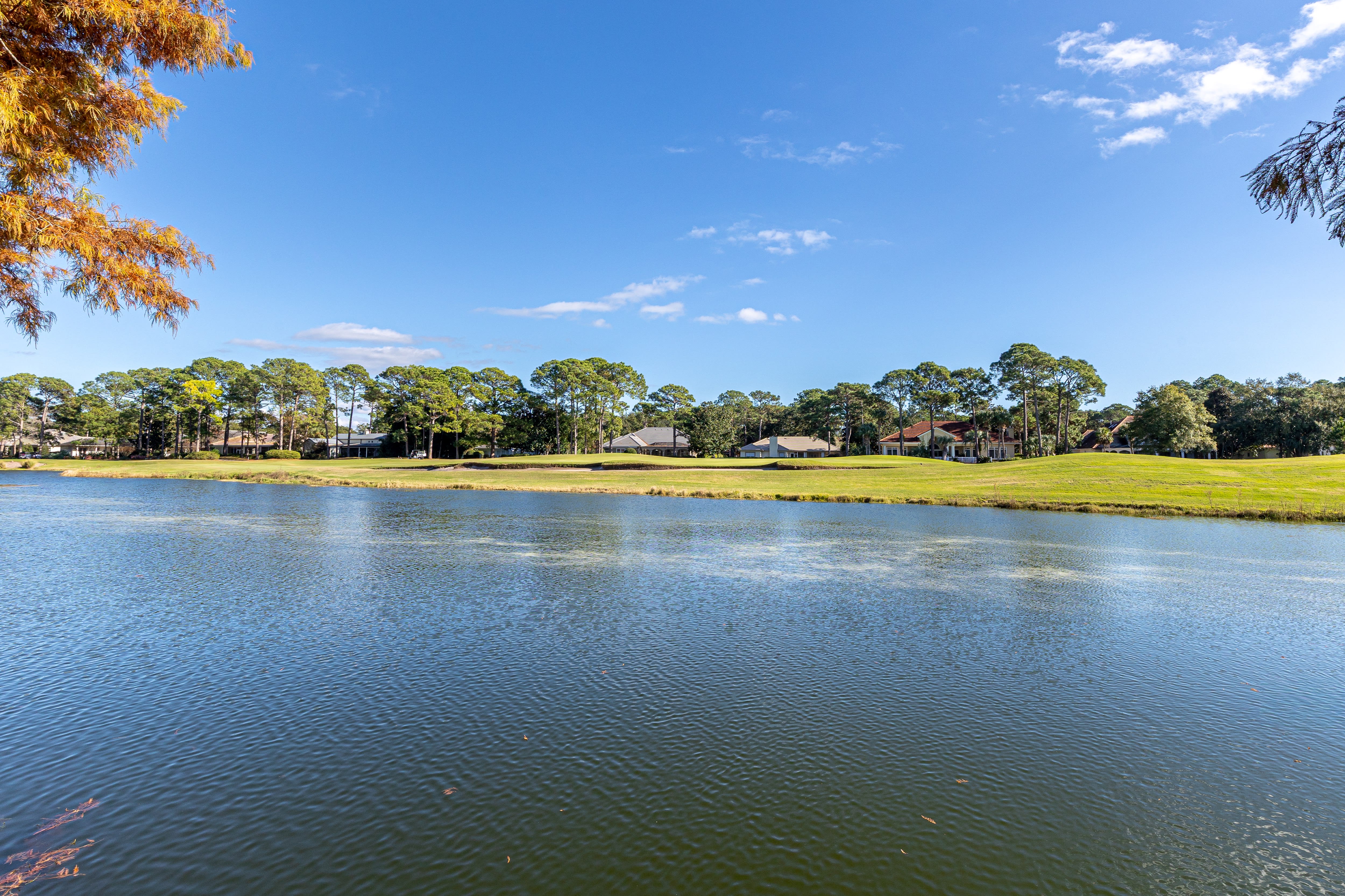 Peaceful lake surrounded by autumn foliage and residential homes creating a serene neighborhood setting.