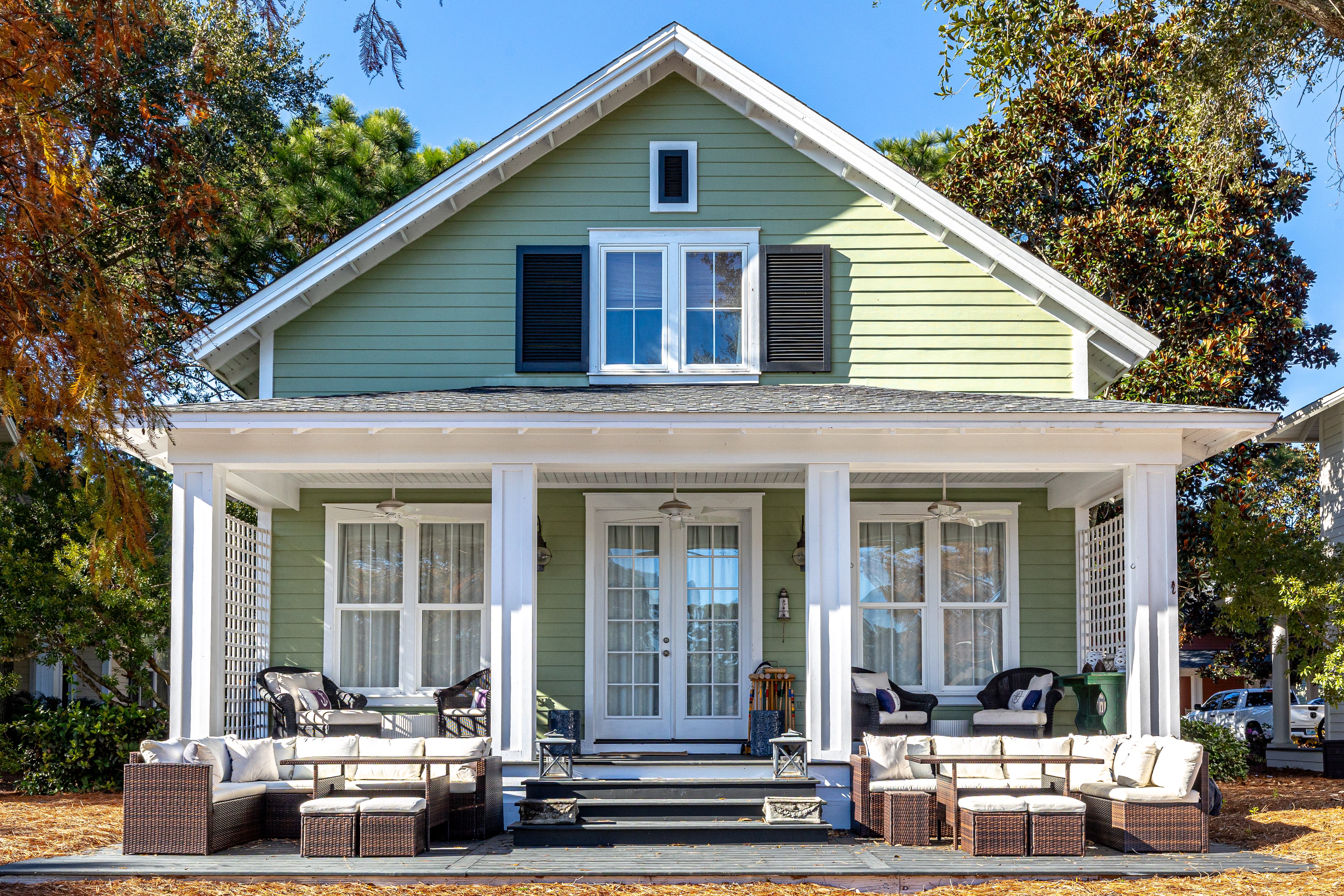 Charming green cottage with wraparound porch featuring comfortable outdoor seating perfect for morning coffee or evening relaxation.