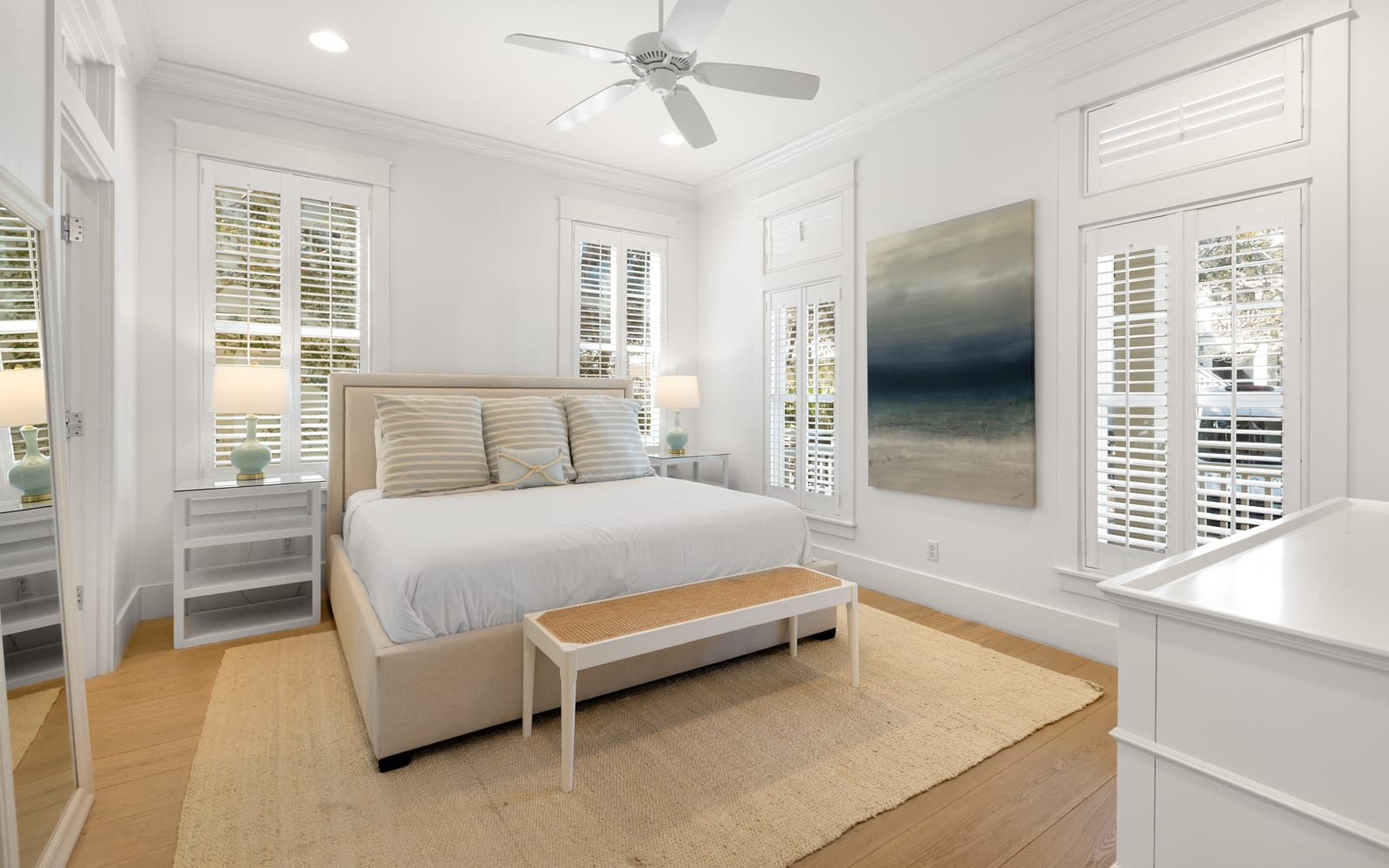 Unwind in your serene coastal bedroom with calming artwork and natural light streaming through shuttered windows.