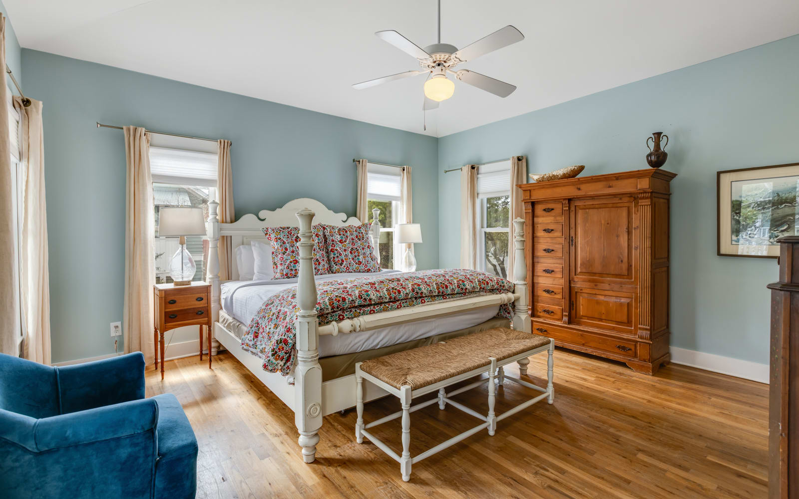 Unwind in your elegant bedroom featuring a plush four-poster bed, rich hardwood floors, and calming blue walls that create a peaceful retreat.