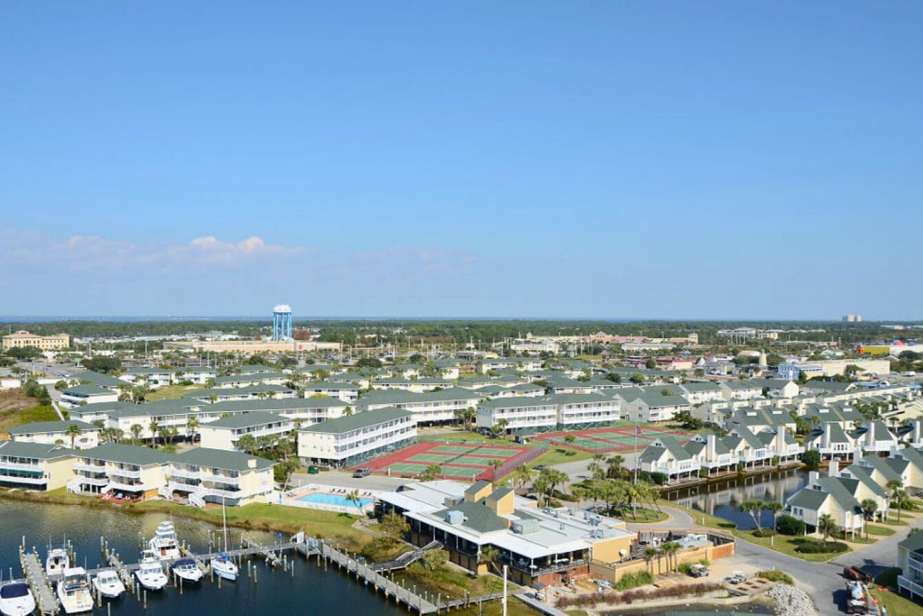 Aerial view of waterfront resort complex with marina, tennis courts, pool facilities and nearby residential community.