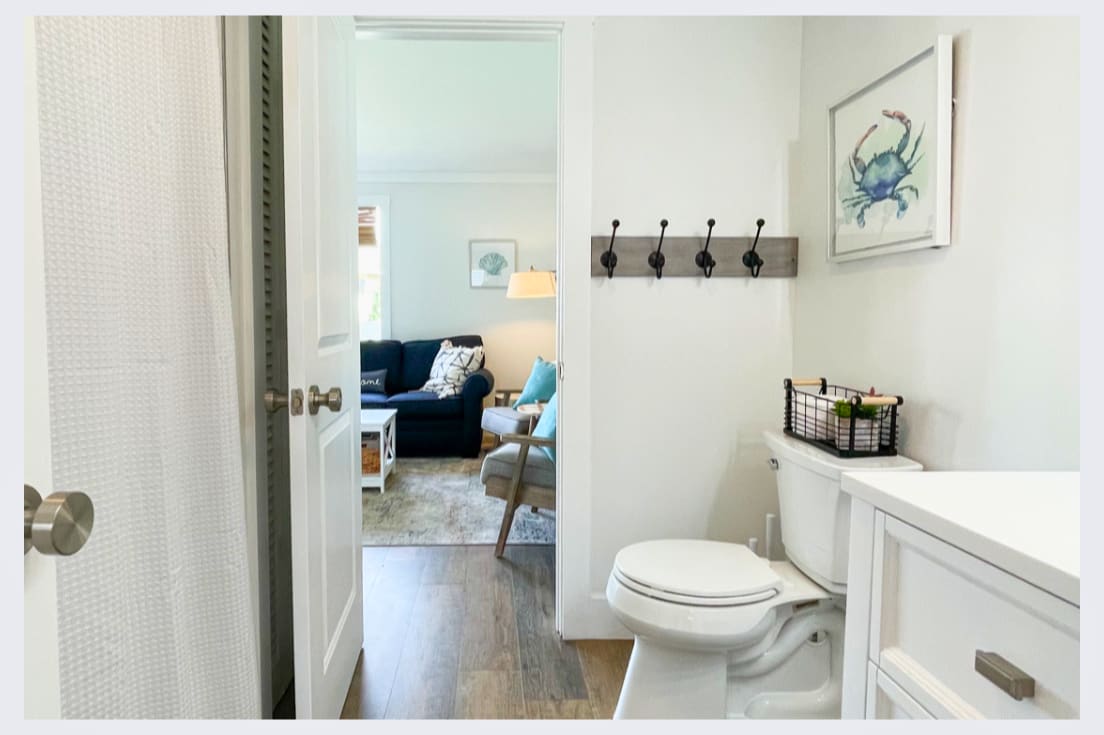 Your private powder room features coastal charm with thoughtful hooks and storage, connecting seamlessly to the bright living space.