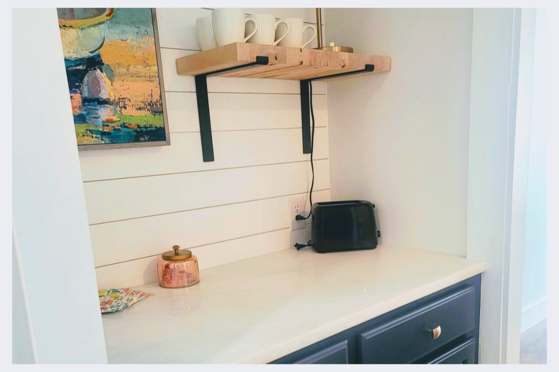 Your charming kitchenette corner features fresh white shiplap walls, a sleek toaster for morning treats, and coffee mugs ready for your perfect brew.