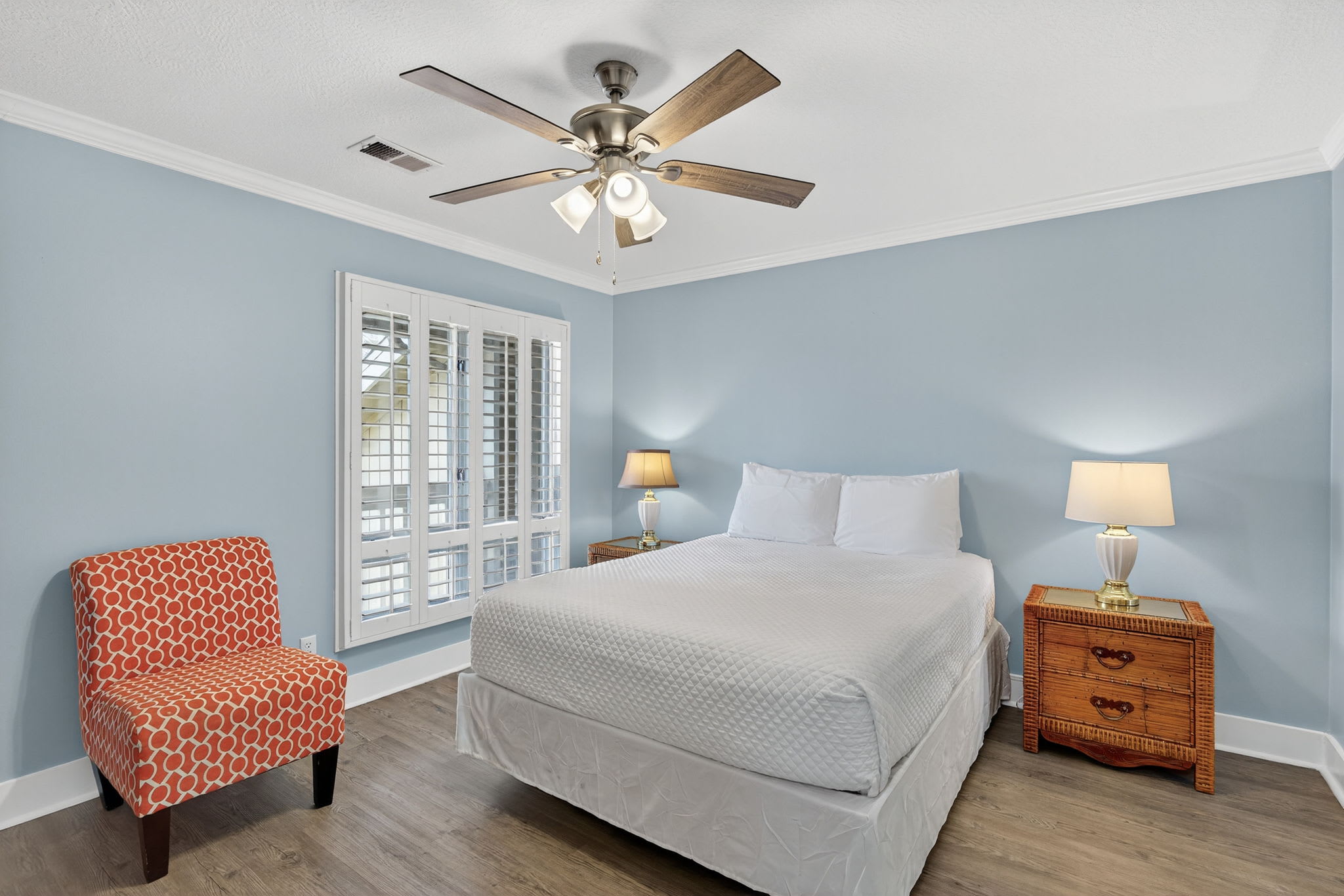 Relax in your peaceful bedroom with soothing blue walls, comfortable seating, and natural light from plantation shutters creating the perfect retreat for rest.