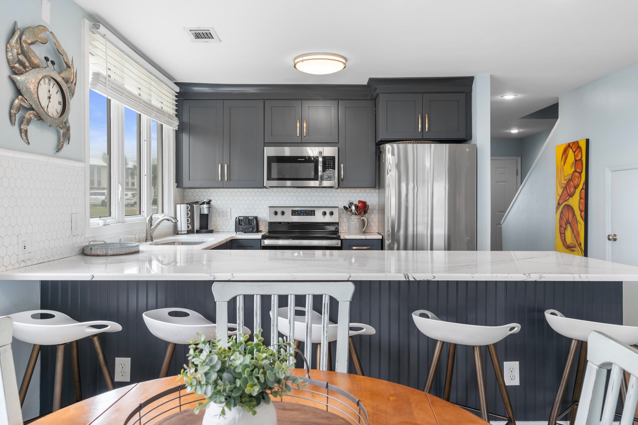 Bright and modern kitchen with sleek navy cabinets, quartz counters, and stainless appliances—bar seating and a cozy dining nook complete the perfect space for gathering.
