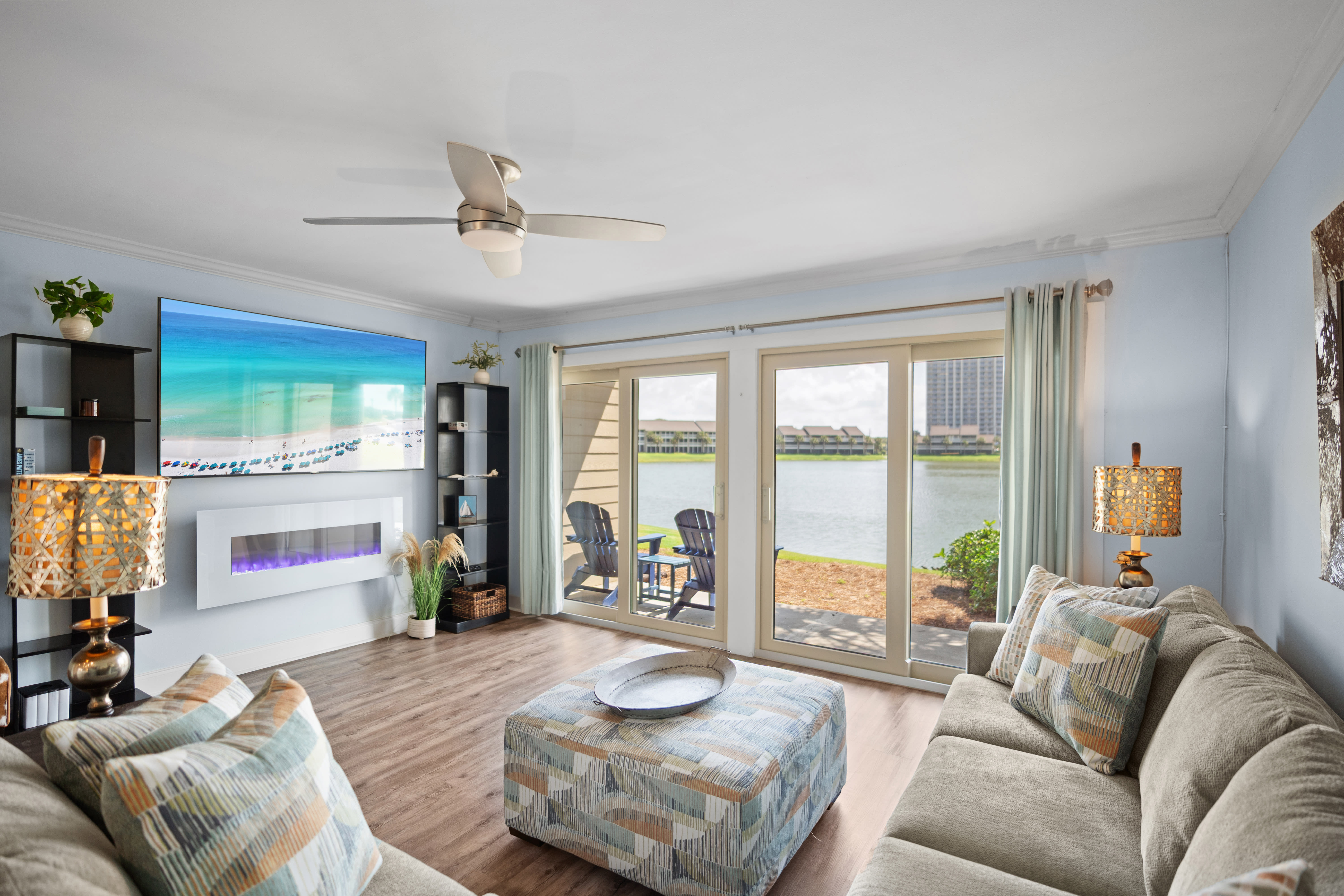Bright lakefront living room with sliding glass doors, modern fireplace, cozy sectional, and LVP wood floors. Relaxed, coastal vibe with patio access and scenic views.