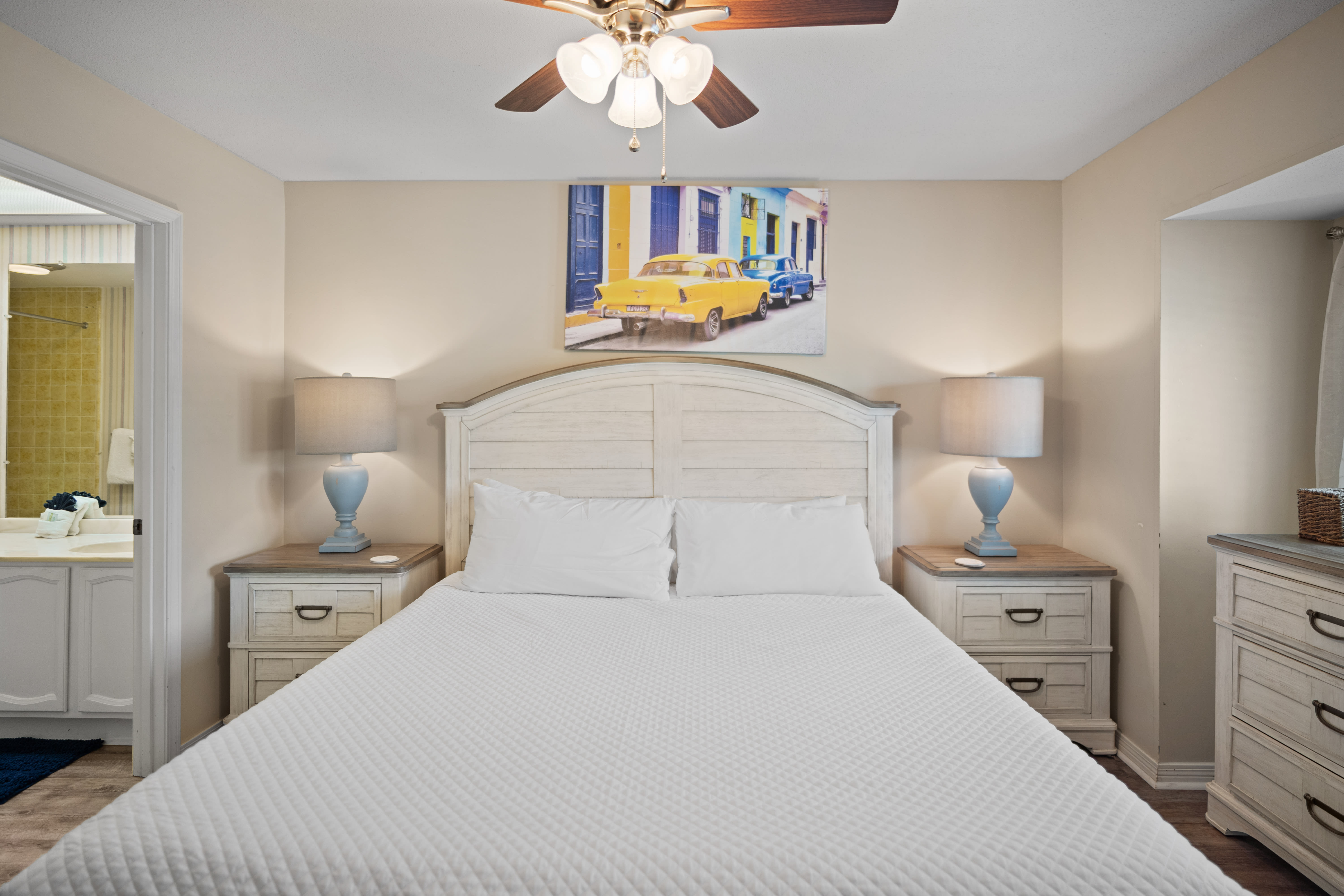 Cozy primary bedroom with a king bed, matching nightstands, and soft lighting from bedside lamps. Features a ceiling fan, neutral walls, and vibrant artwork for a warm, inviting atmosphere.