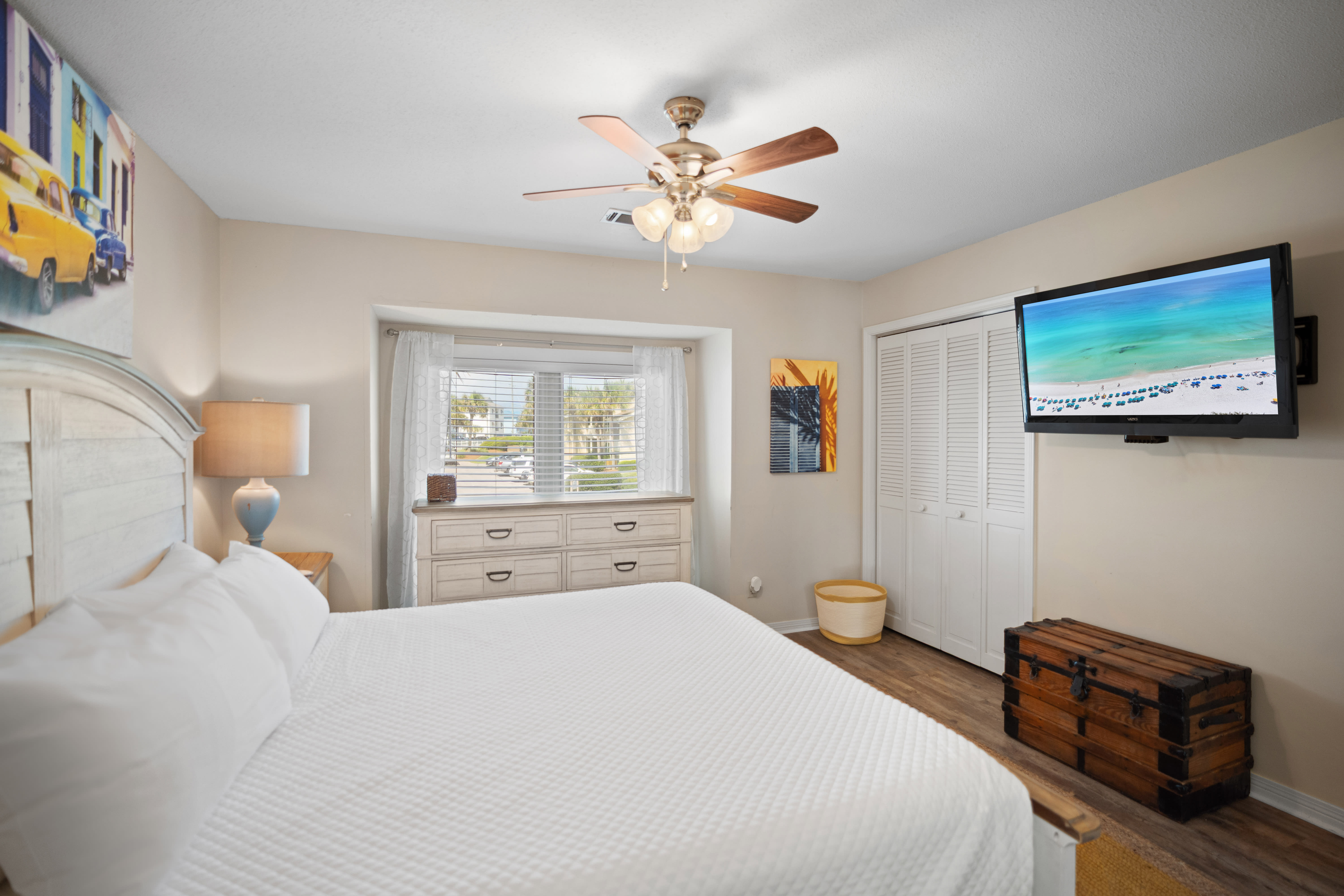 Includes a wall-mounted TV, neutral tones, and warm wood flooring for a relaxed retreat.