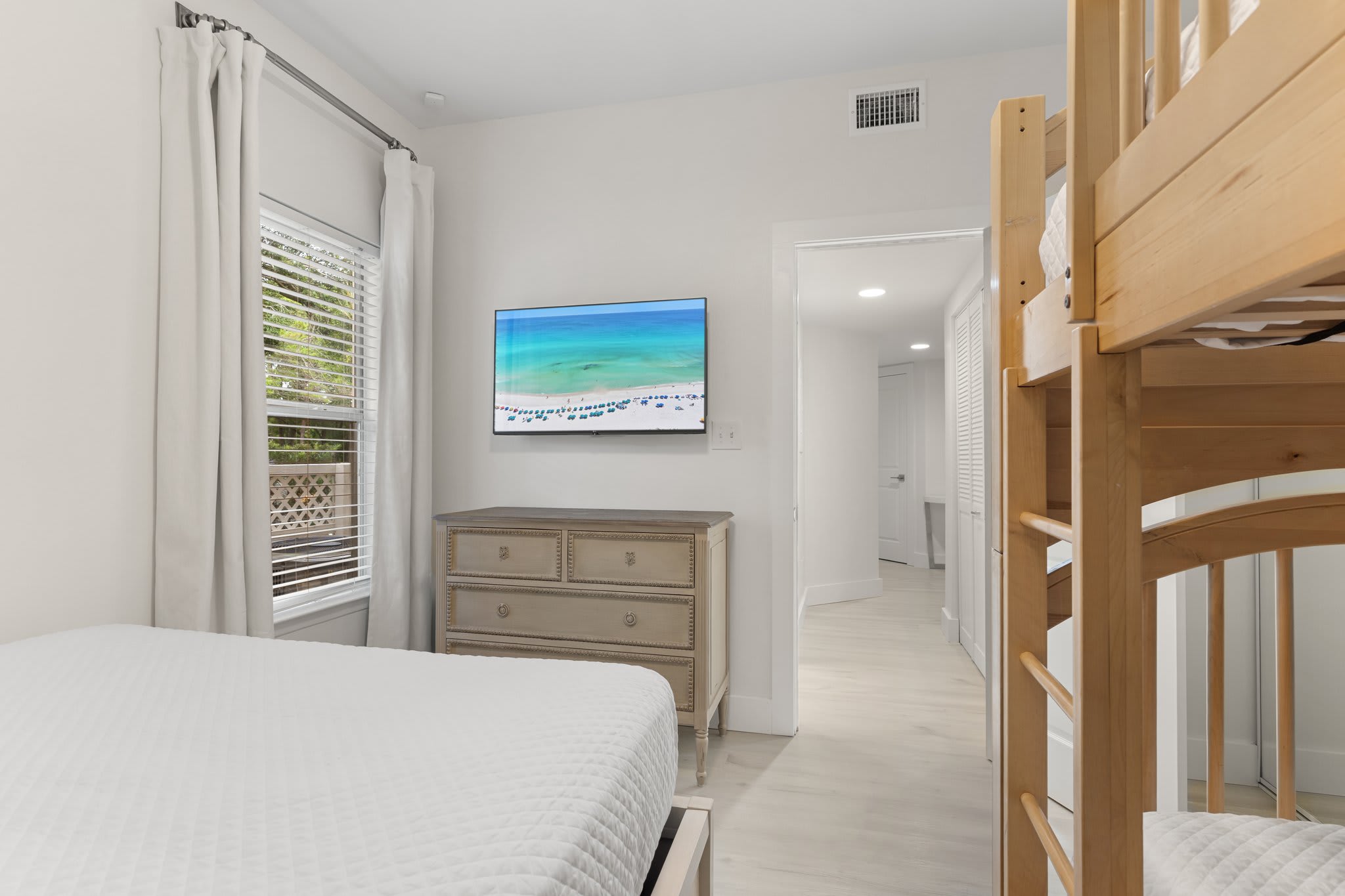 The guest room includes a queen bed, twin bunks, a flat-screen TV, and soft natural light for a restful stay.