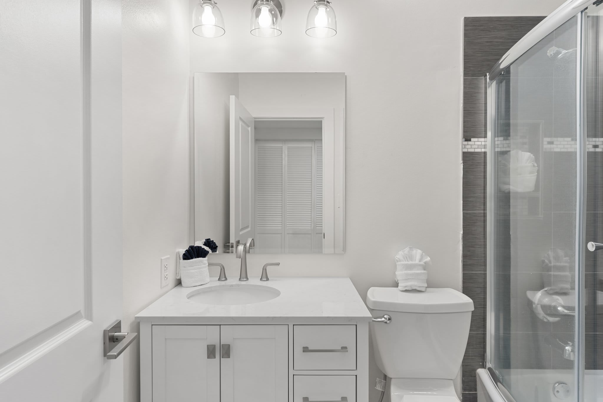 This modern guest bathroom features a crisp white vanity, sleek fixtures, and a tiled tub/shower combo.
