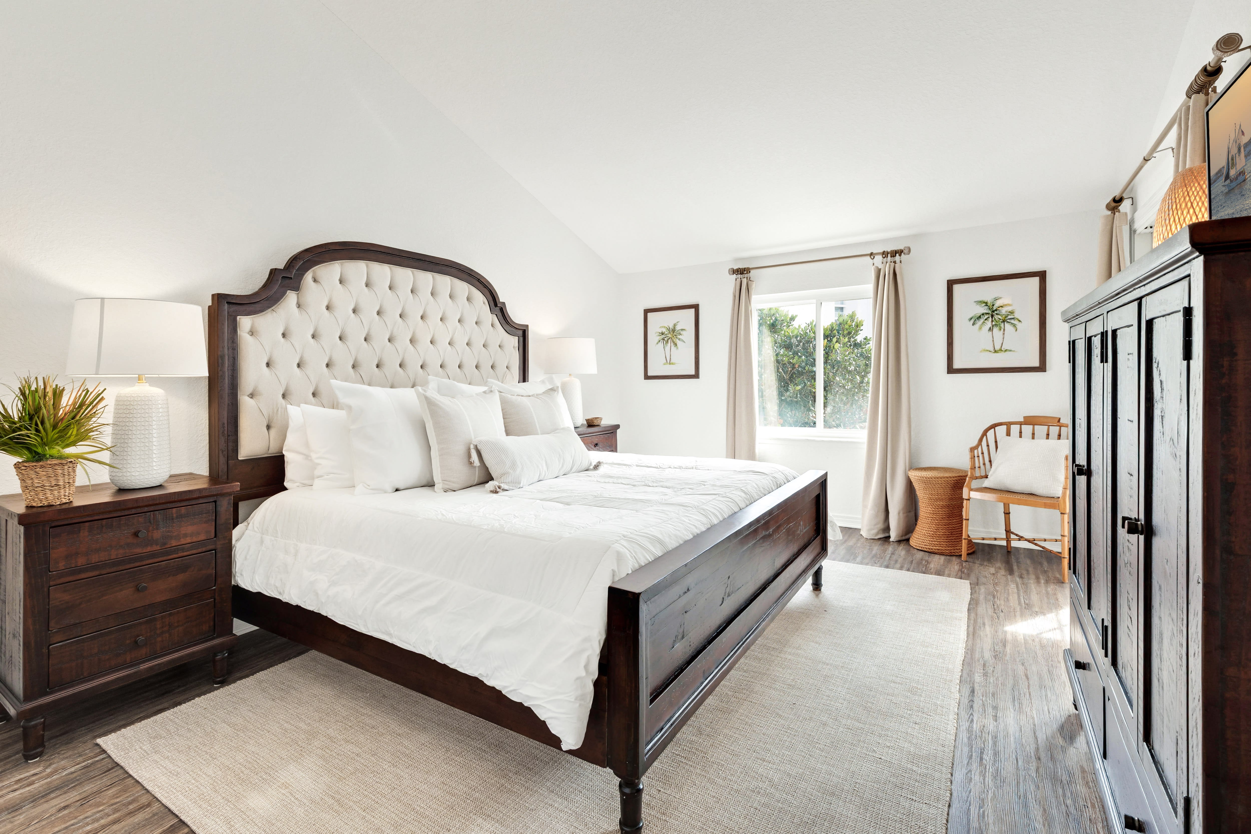 Sink into crisp white linens and a plush tufted headboard in your serene bedroom, complete with warm wood furnishings and tropical artwork.