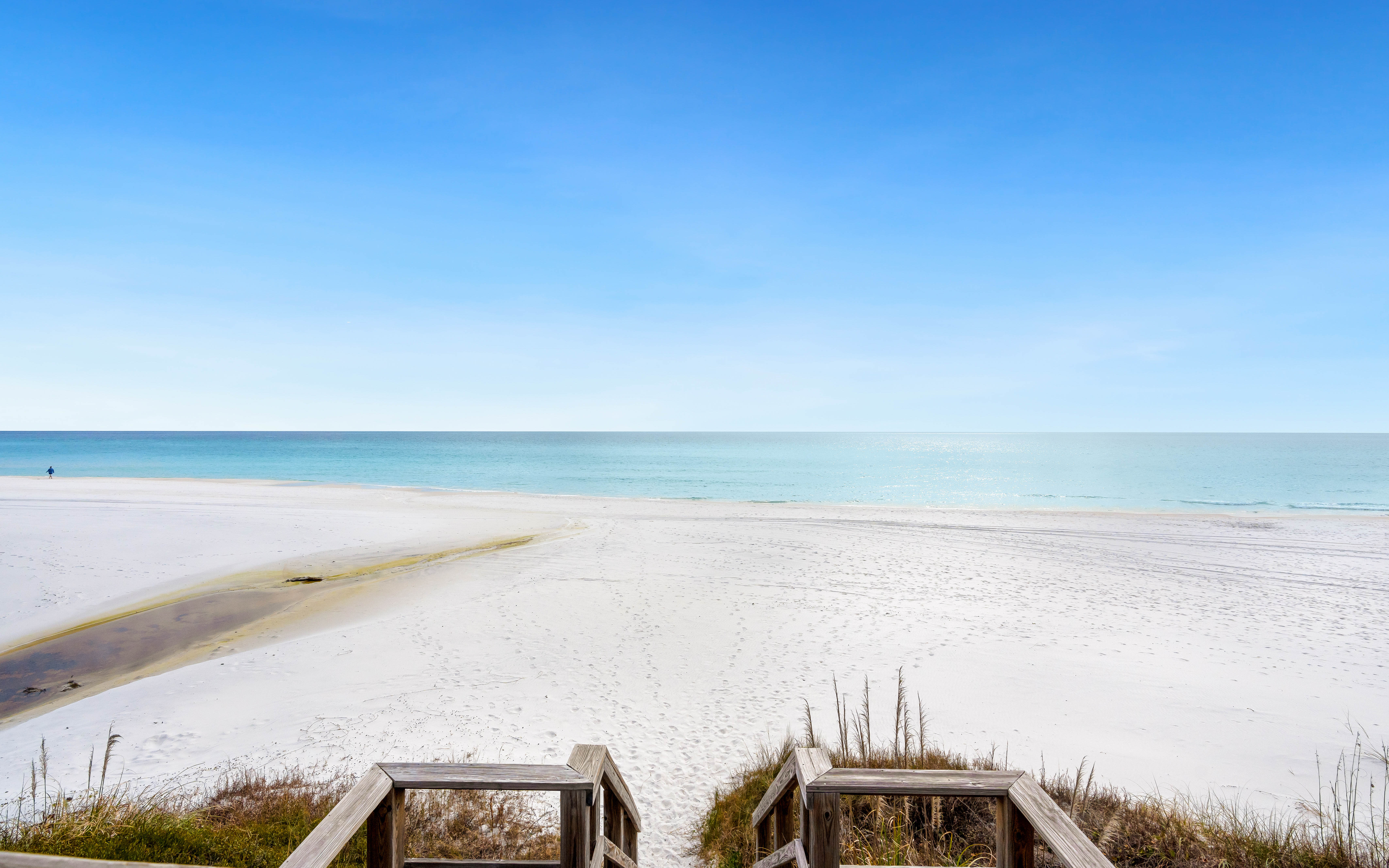 Pristine white sand beach meets crystal-clear turquoise waters under an endless blue sky, accessed by charming wooden walkway.