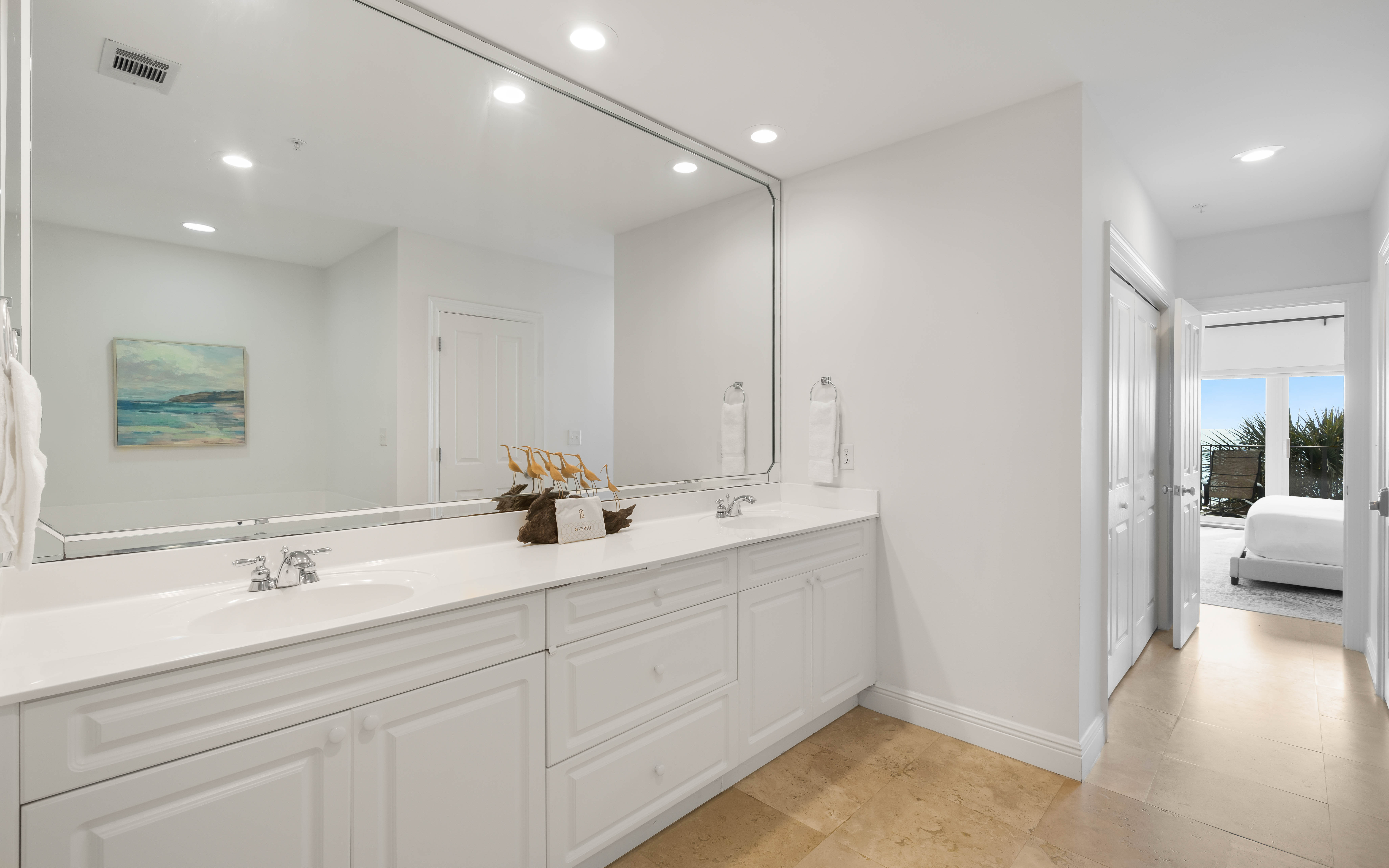 Your luxurious bathroom features dual vanities with pristine white cabinetry, elegant marble countertops, and a large mirror perfect for your morning routine.