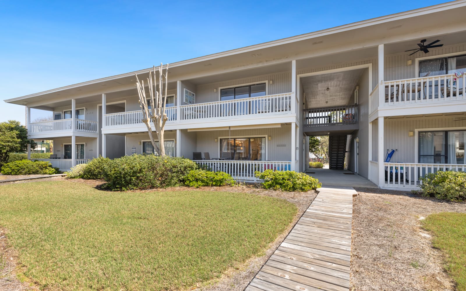 Charming two-story building with white railings and walkway, surrounded by manicured lawns and landscaping under clear blue skies.