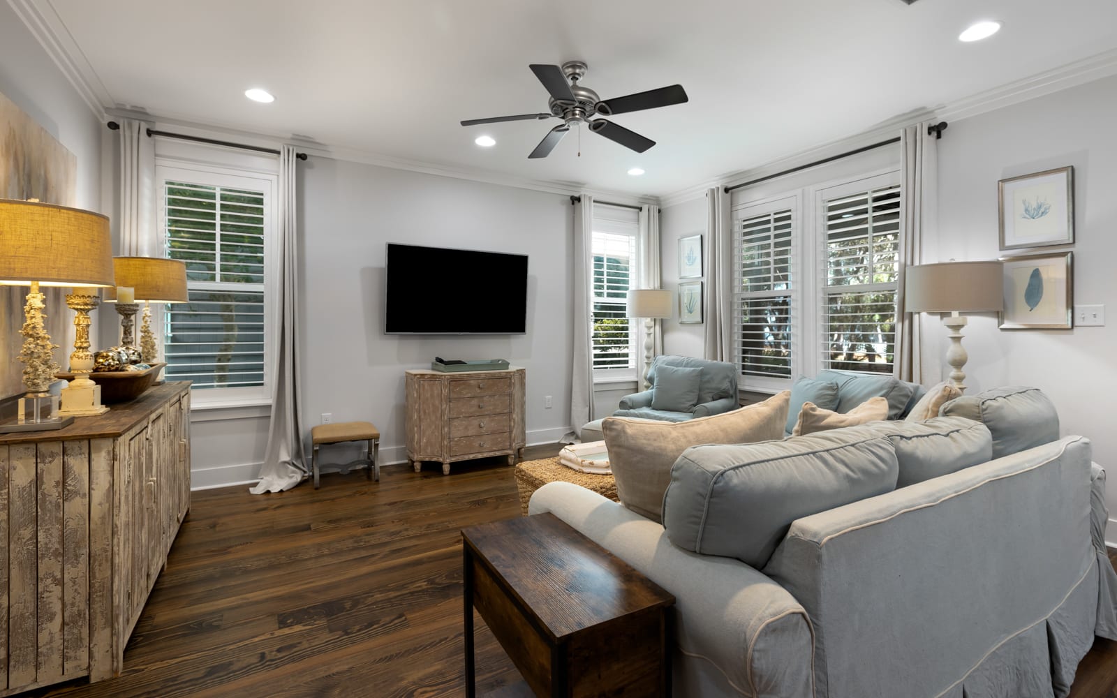 Sink into plush seating in your bright living space, where natural light flows through shuttered windows and coastal decor creates a serene retreat.