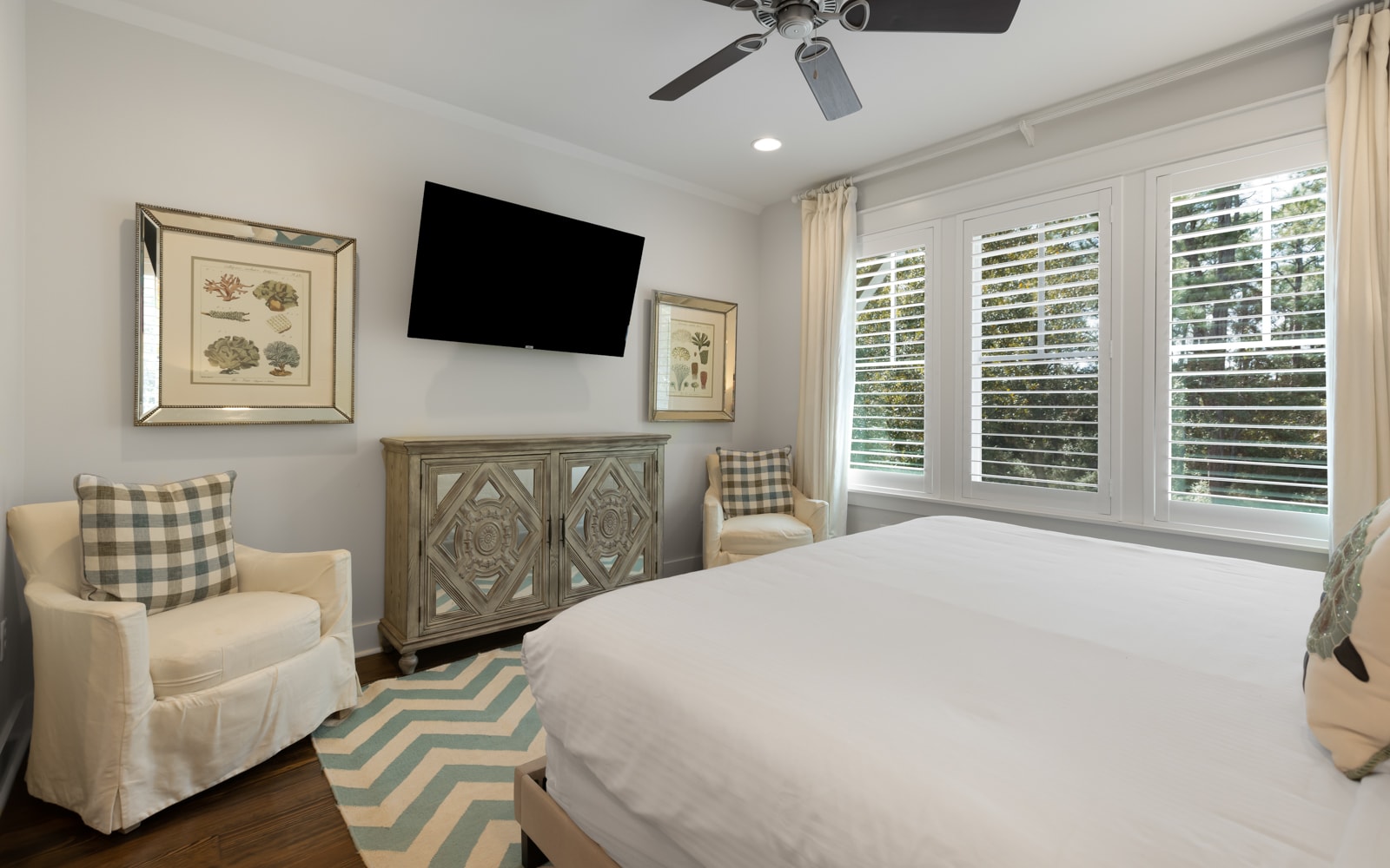 Relax in your peaceful bedroom with cozy seating, entertainment, and soft natural light streaming through plantation shutters.