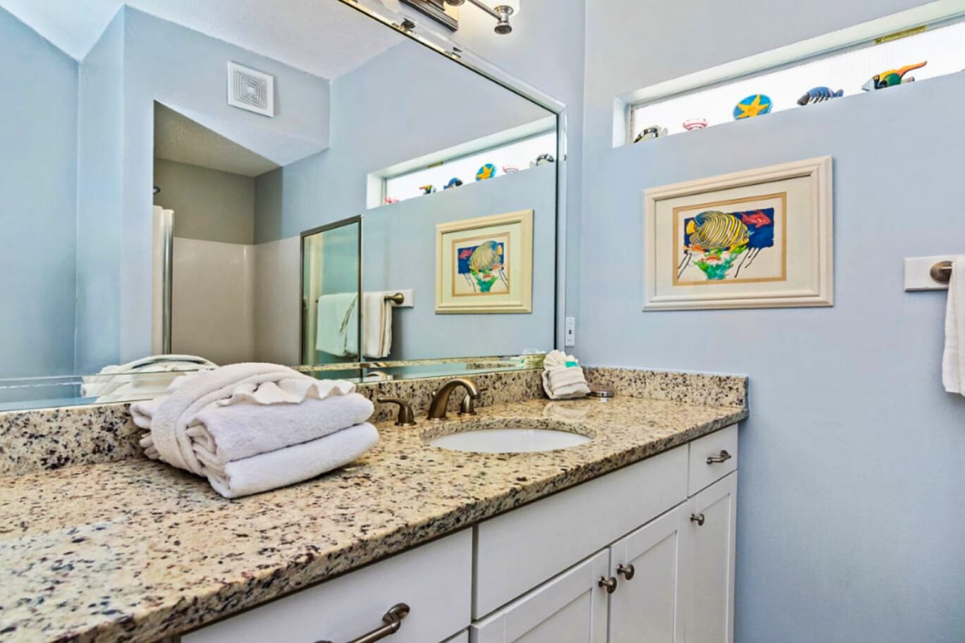 Bright coastal bathroom with granite vanity, double sinks, soft beach décor, and a clean, calming design perfect for refreshing after a day at the beach.