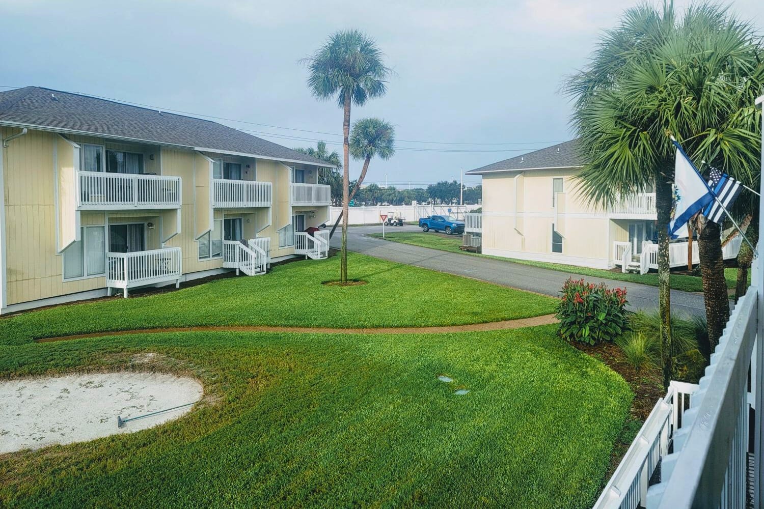 Tropical resort buildings feature white balconies amid lush palm trees and manicured lawns in this peaceful Florida-style setting.