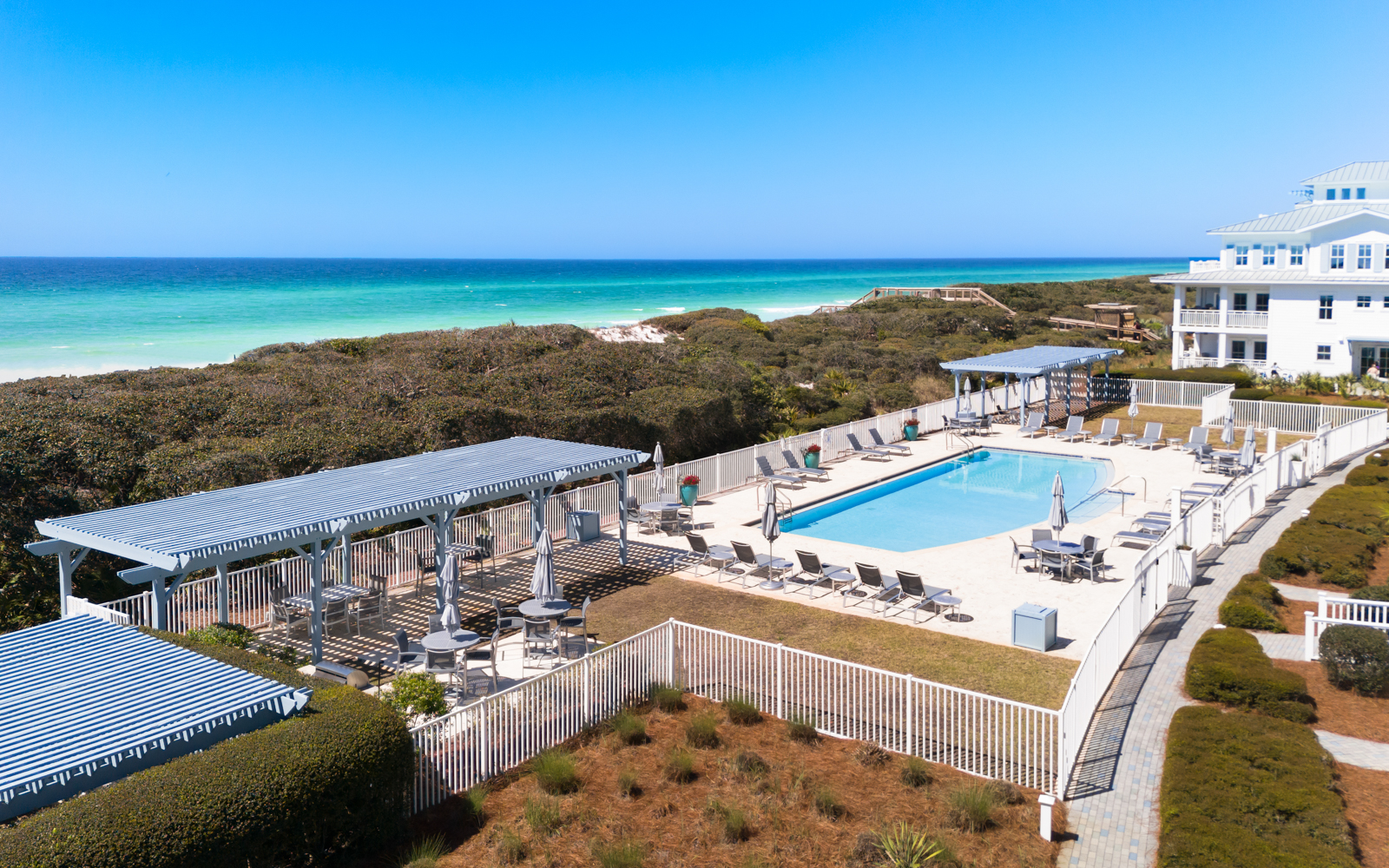 Beachfront property featuring elevated pool deck with pristine white sand beach and turquoise waters beyond natural dune vegetation.