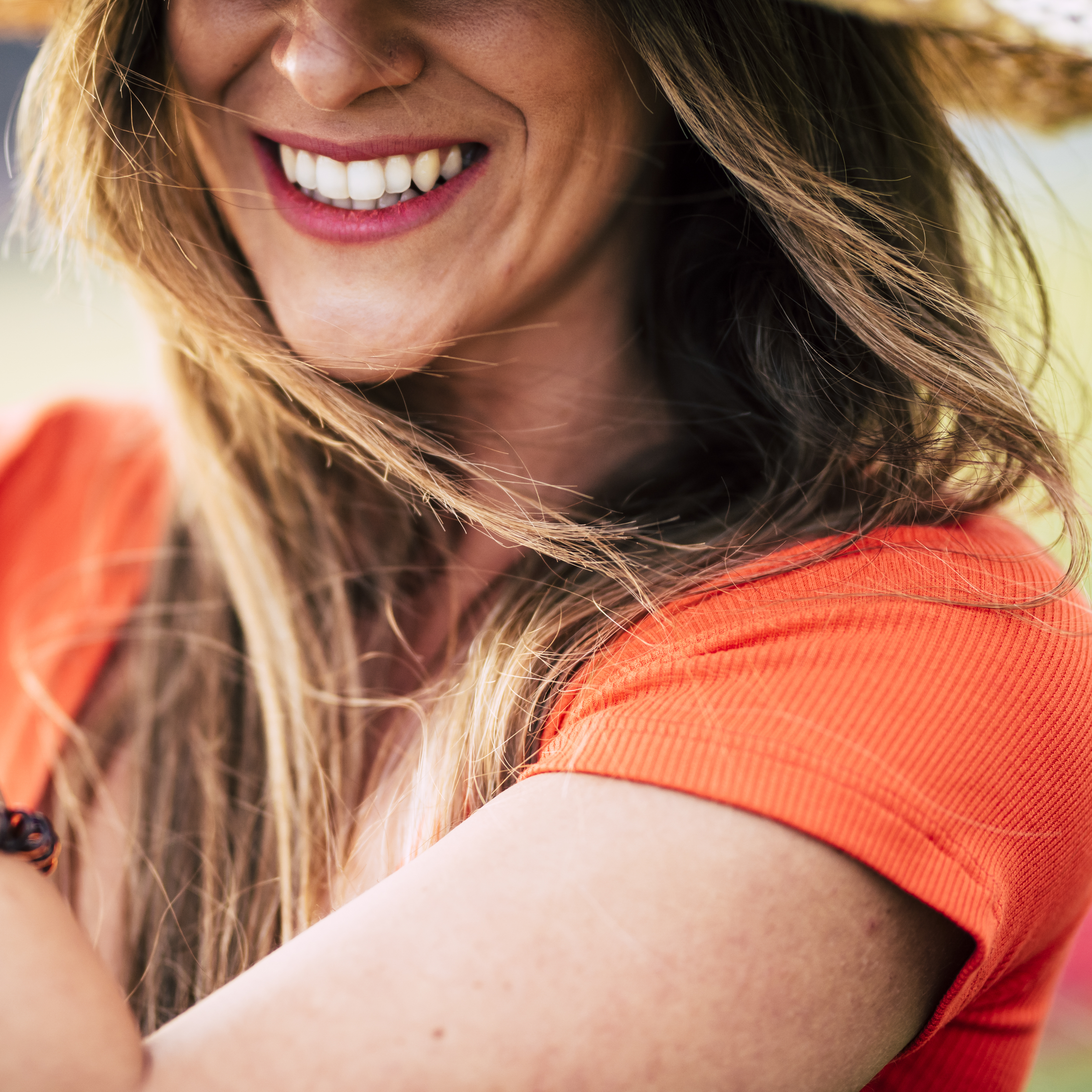 Fotografía de una mujer sonriendo en la que solo se ve su nariz y sus dientes blancos junto a sus hombres y el pelo castaño