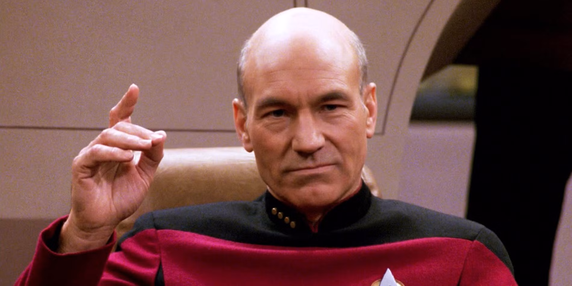 Sir Patrick Stewart en su papel de Jean-Luc Picard sntado en su silla de mando con la mano levantada antes de decir Engage!