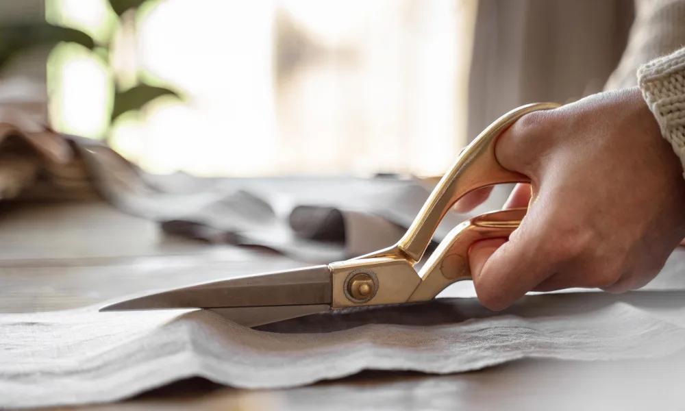 carefully using scissors to cut and prepare a premium textile to be made into custom drapery