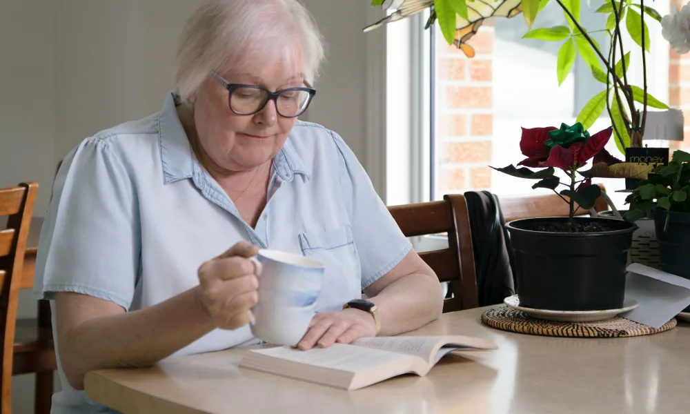 marilyn sitting at her eat in kitchen, drinking morning tea while reading a book