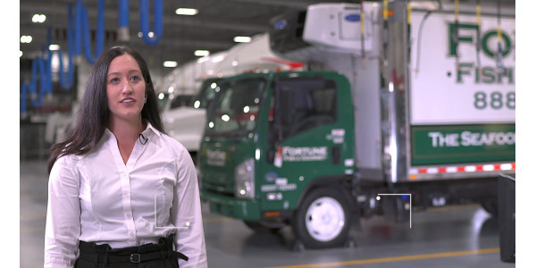 Woman speaking to the camera with a green refrigerated truck on the background