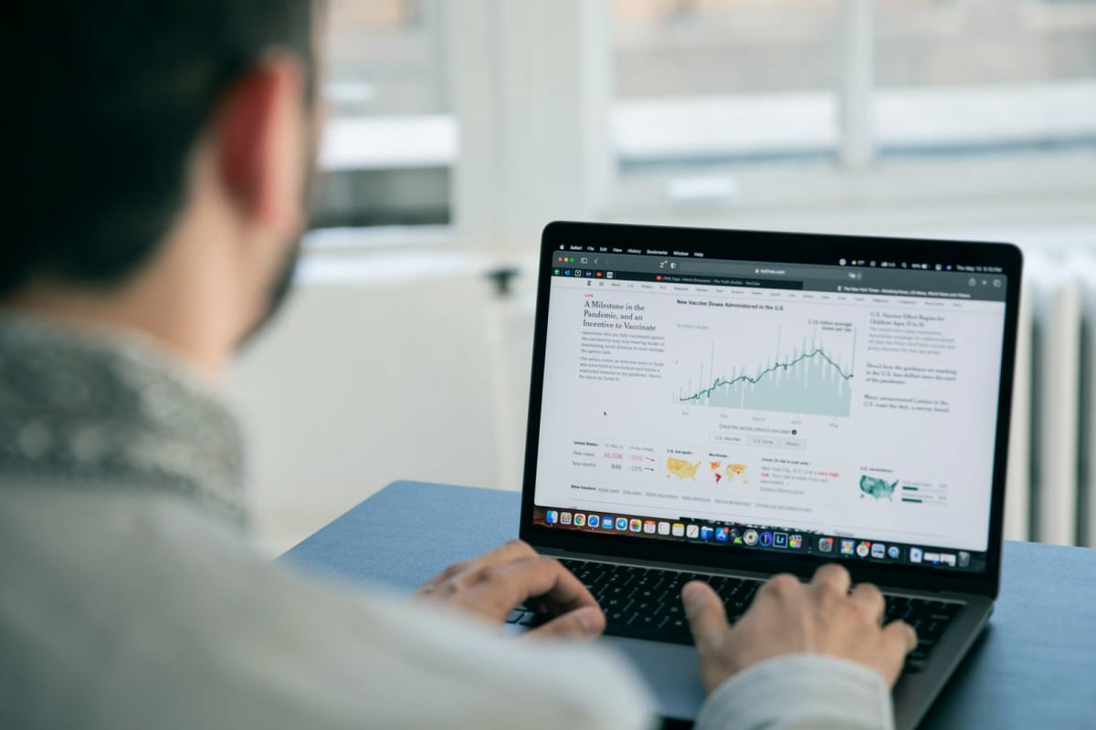 Persona de espaldas usando una laptop que muestra una página con un gráfico de datos, junto a una ventana